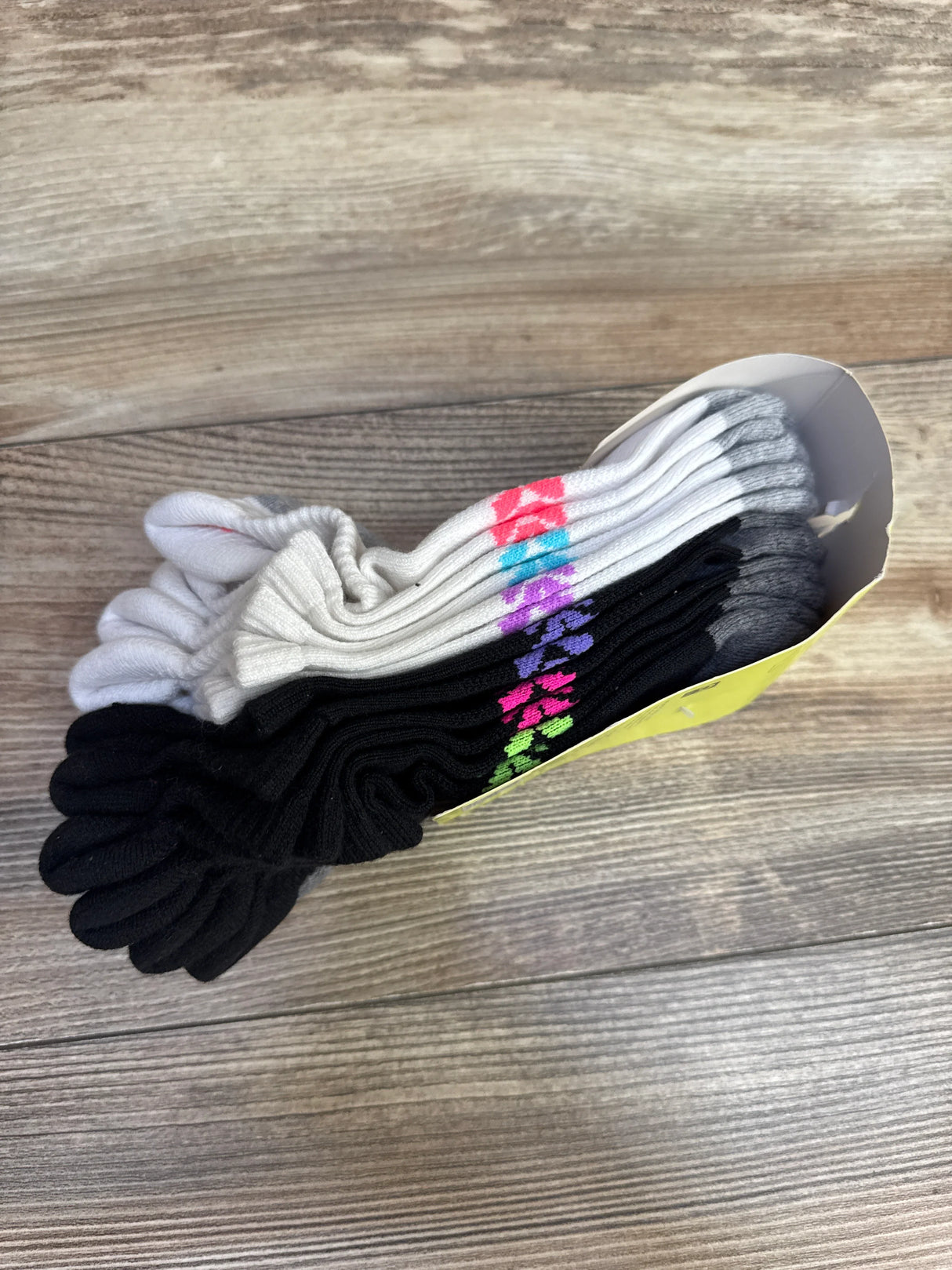 Angled top view of All In Motion no-show socks 6-pack showing black and white pairs with multicolor diamond accents on wood