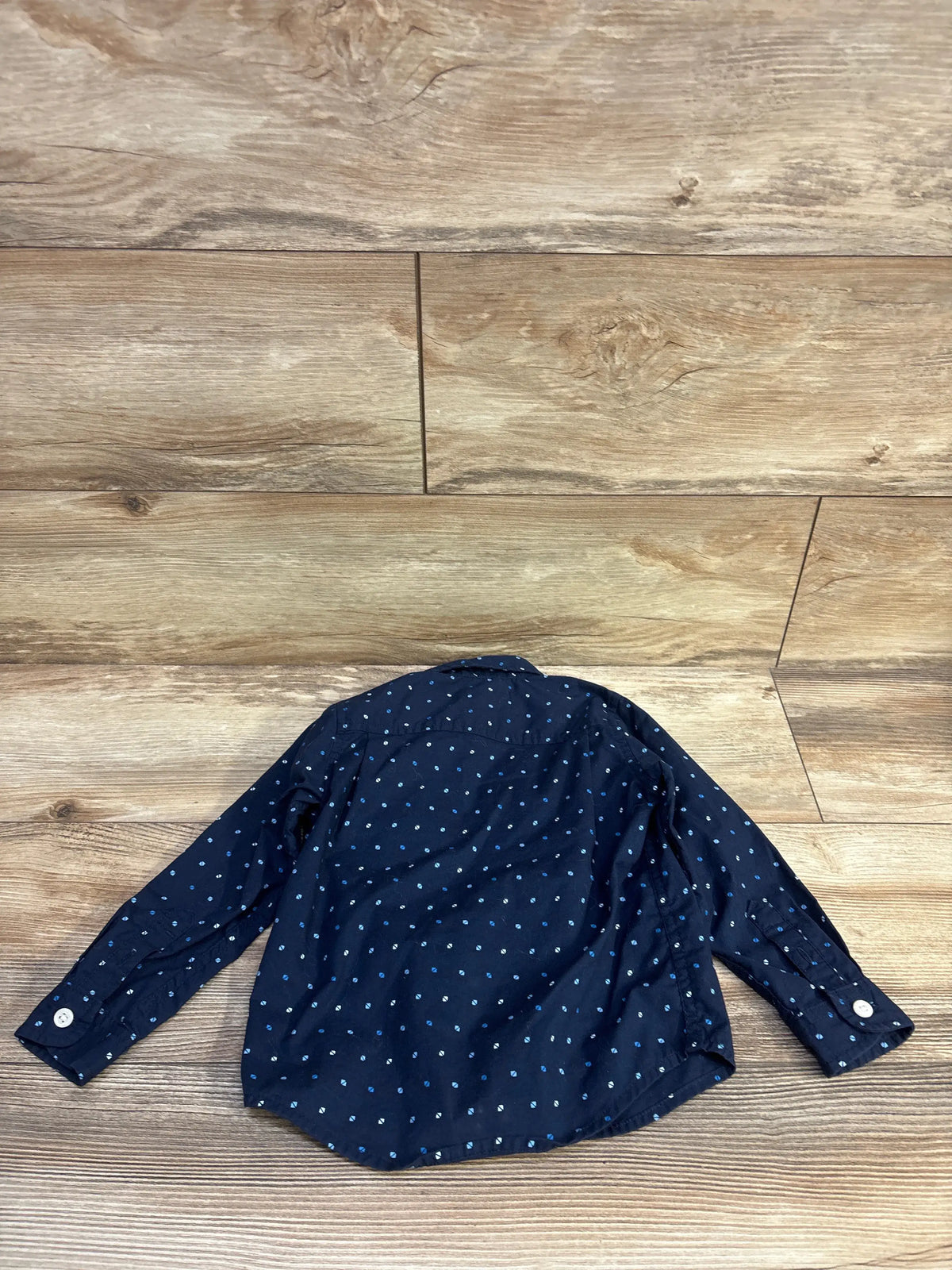 Navy blue button up shirt with white and blue polka dots for toddlers on a wood background