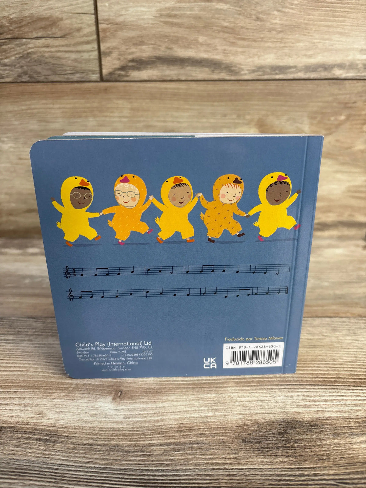 Back of Cinco Patitos / Five Little Ducks board book with children in yellow duck costumes and musical notation on wooden floor