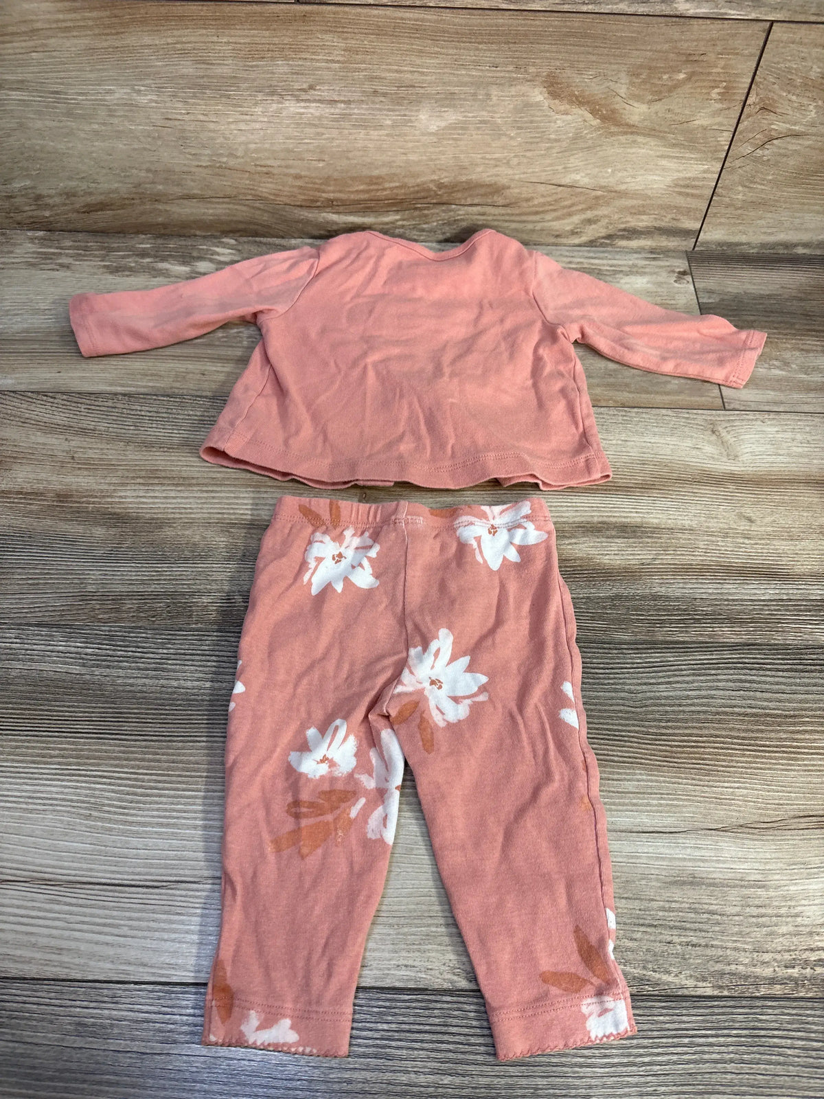 Top-down view of Carter’s pink two-piece button-front baby set with long sleeves and white floral bottoms on wood grain