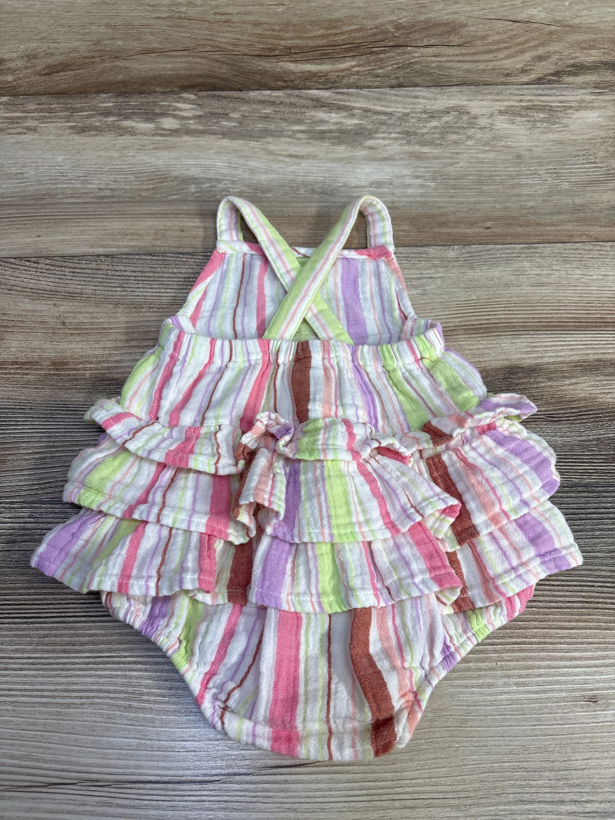 Flat lay of Okie Dokie ruffle romper size 6M showing pastel striped fabric and tiered ruffles on wood background