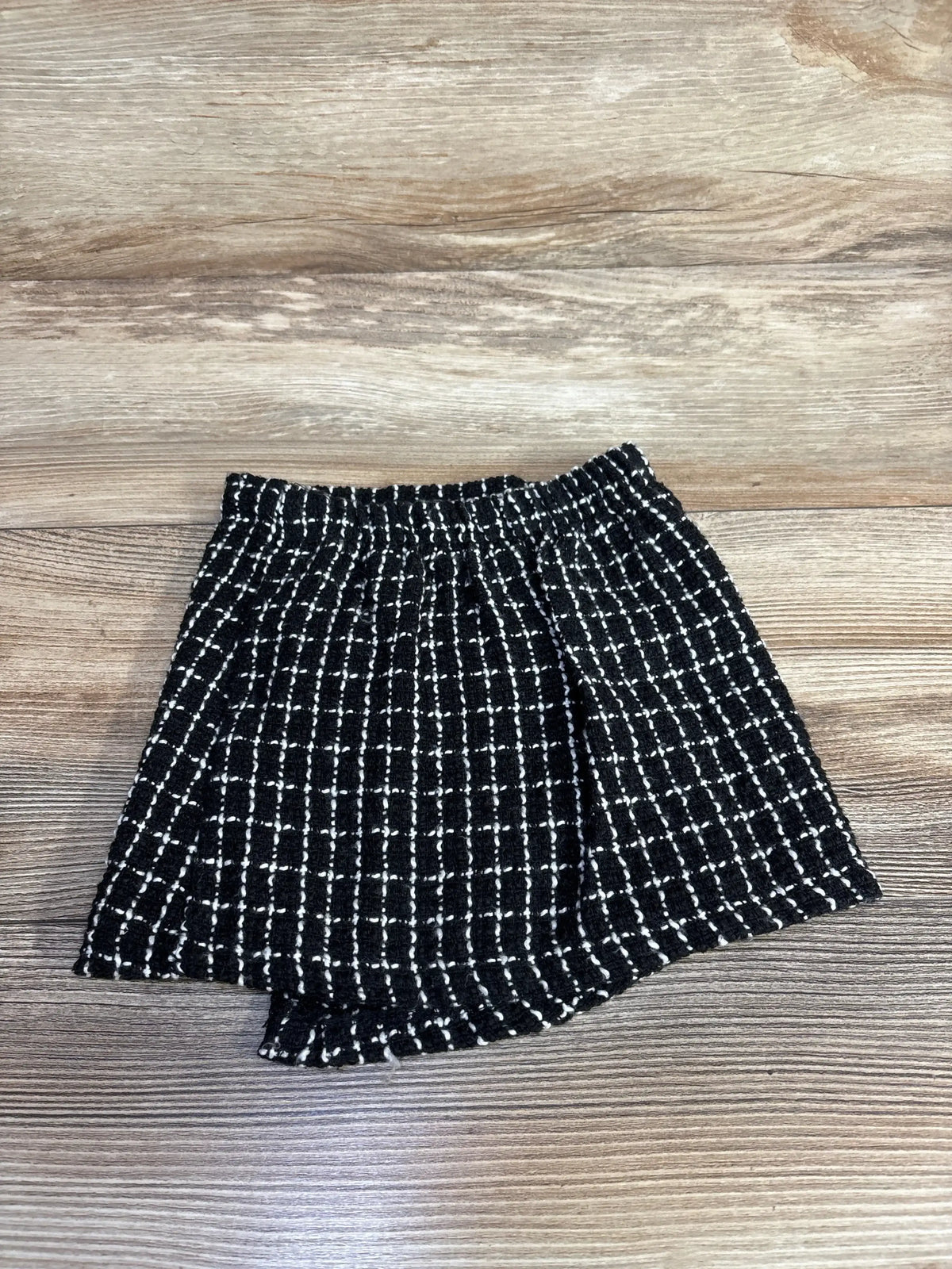 Flat lay of tweed button-up mini skirt size 9-12m with elastic waistband and black-and-white check pattern on wood floor