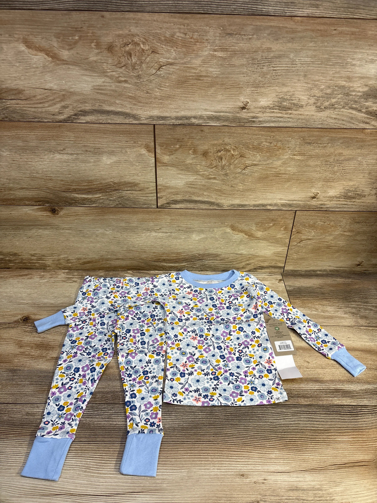 Flat lay of Honest Baby 2-piece organic toddler pajama set showing floral print and blue cuffs on wood background