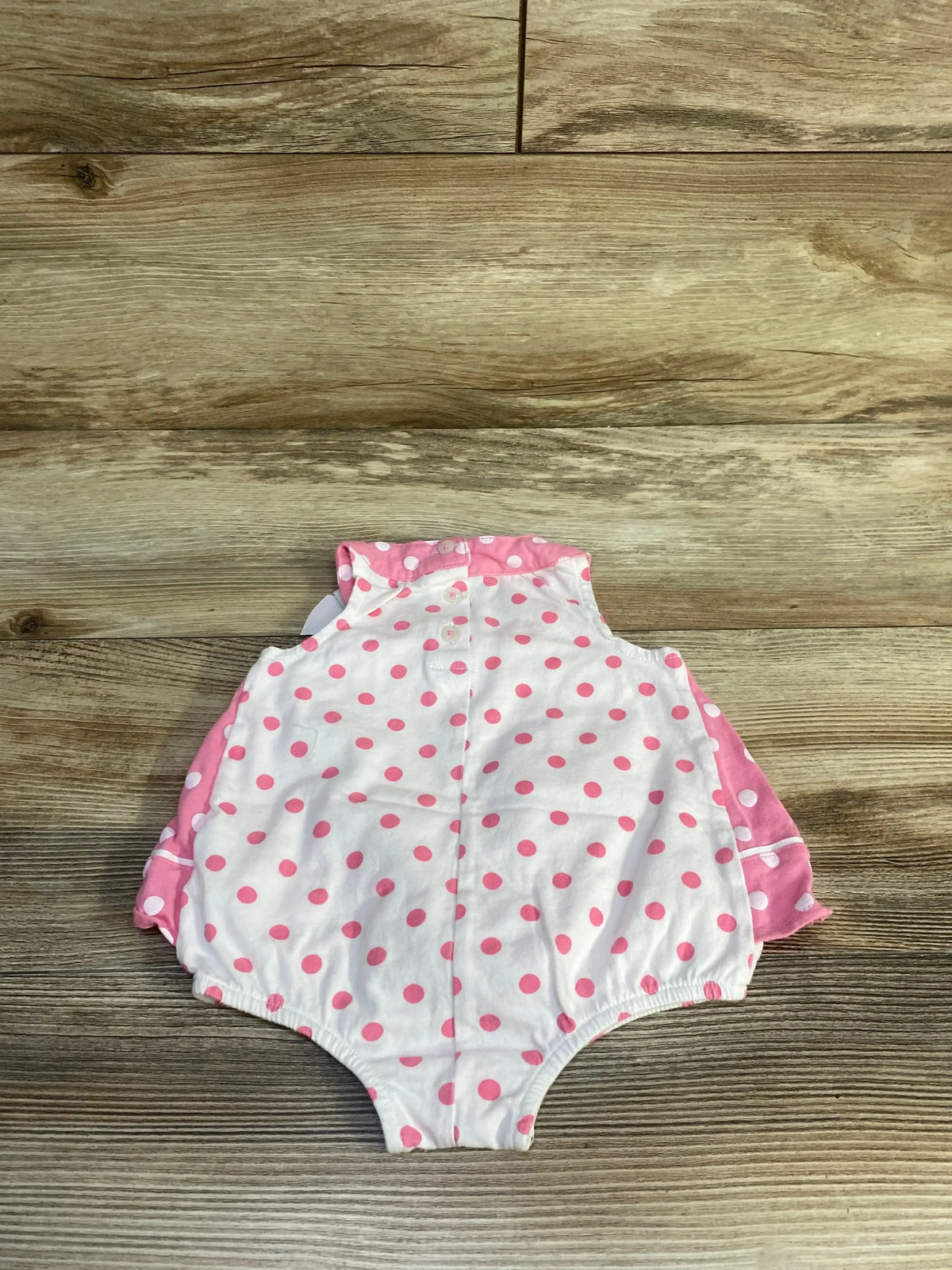 Front view of First Impressions polka dot bow bodysuit dress in pink, size 3-6m, with bow and sleeveless design on wood