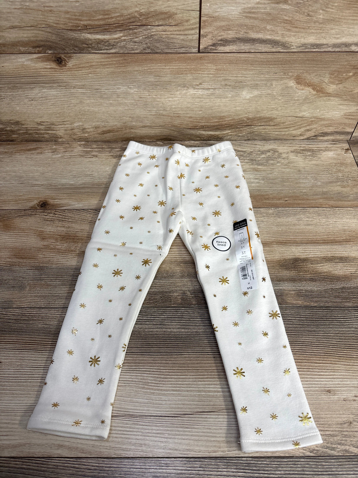 White kids fleece-lined leggings with gold star print on wooden floor background