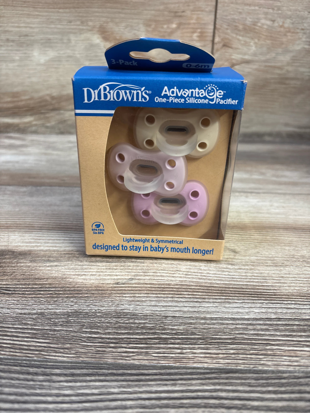 Front view of Dr. Brown’s one-piece silicone pacifier 3-pack (0–6m) showing three pastel pacifiers in box on wood surface