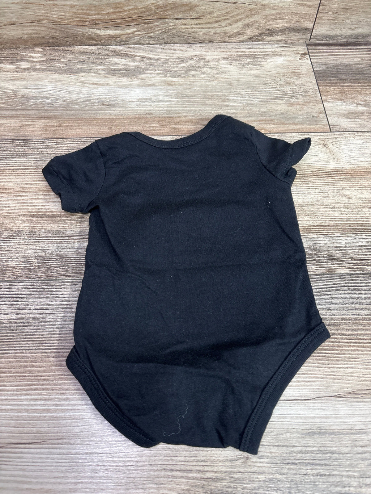 Back view of a plain black Nike bodysuit for infants, size 6m, on a wooden background.
