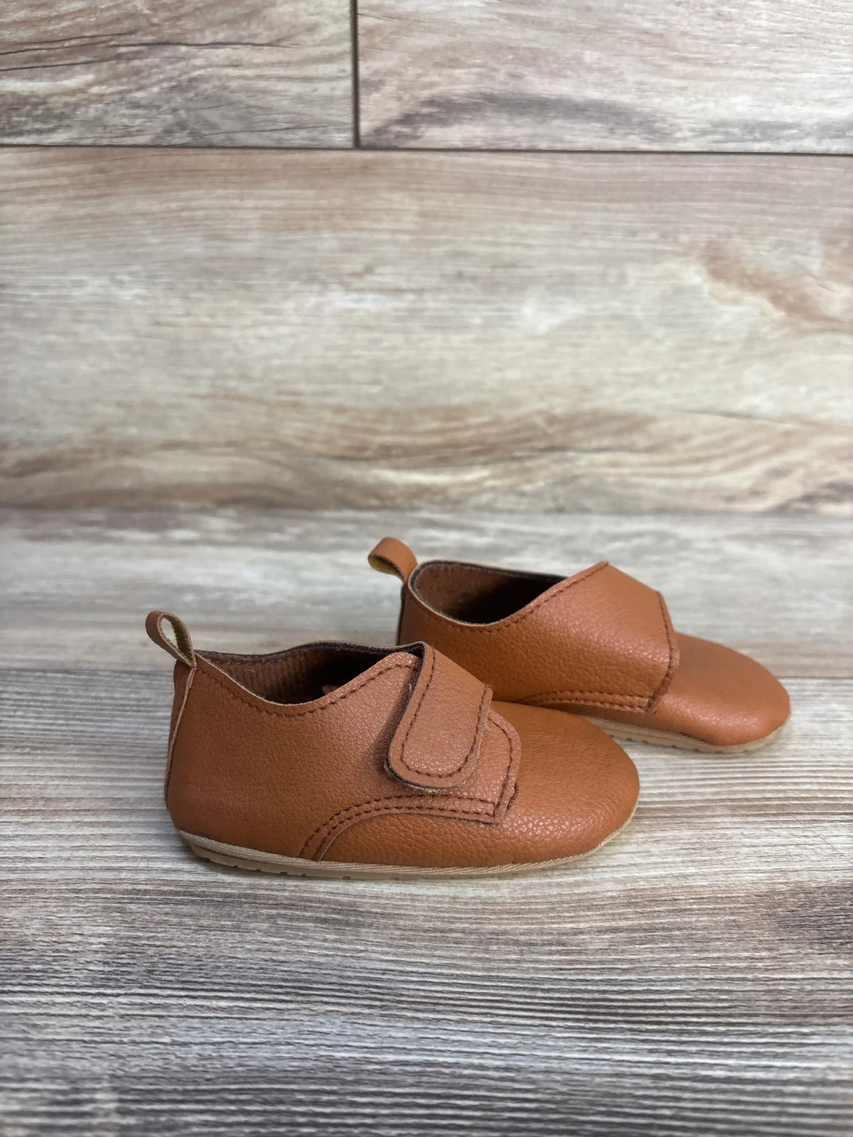 Side view of Baywell brown faux leather first walking soft sole shoes with hook and loop closure and pull tab on woodgrain
