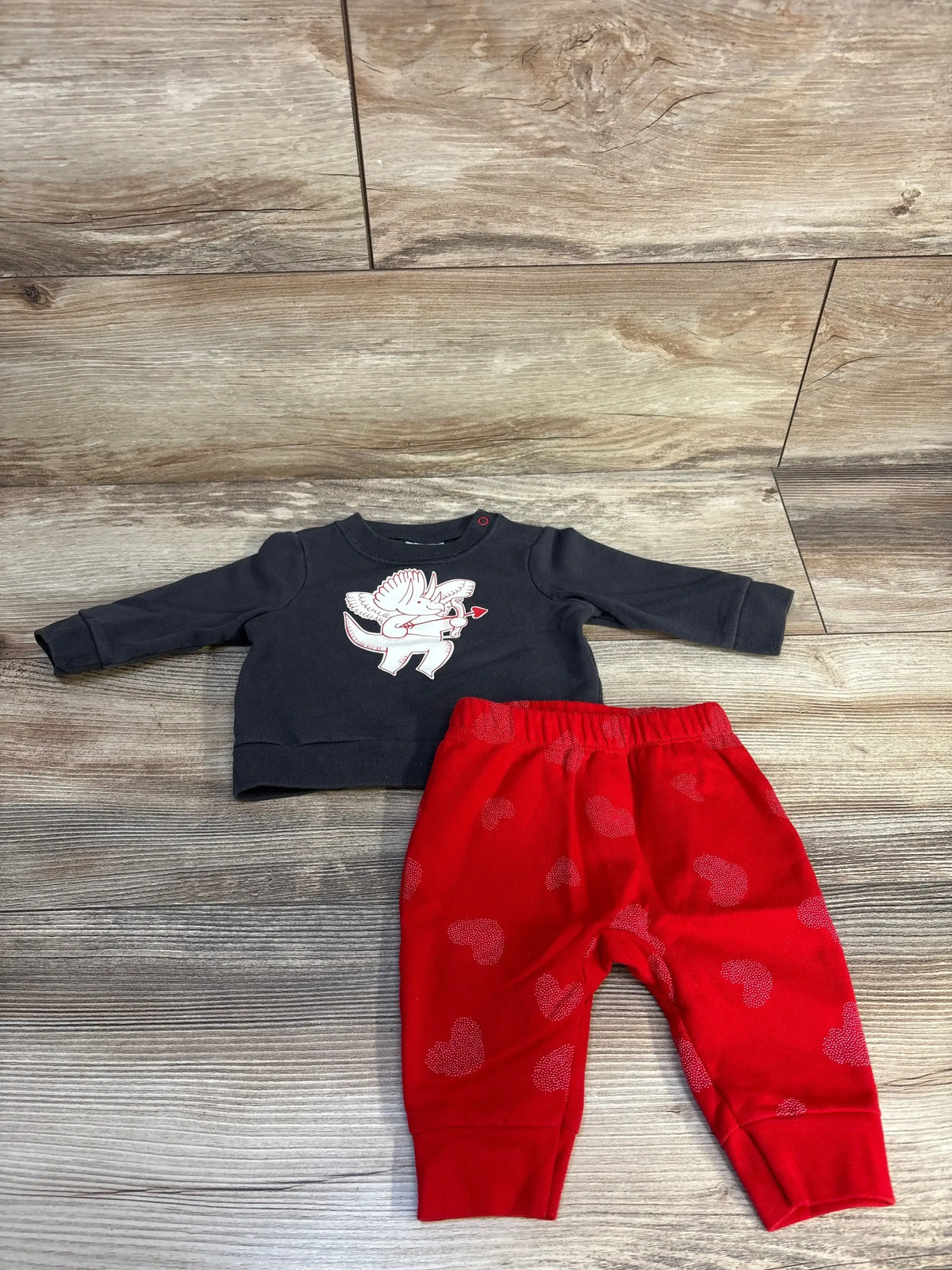 Flat lay of newborn Cat & Jack sweatshirt and heart-print pants showing cupid dino graphic on grey top on wood floor