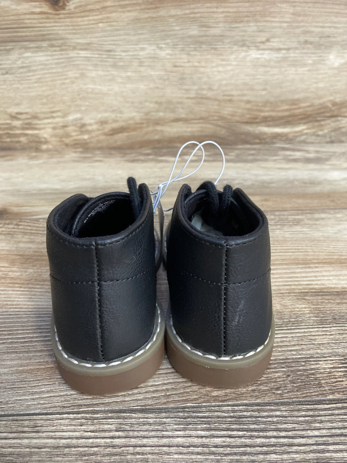 Back view of black toddler boots with brown soles on wooden background