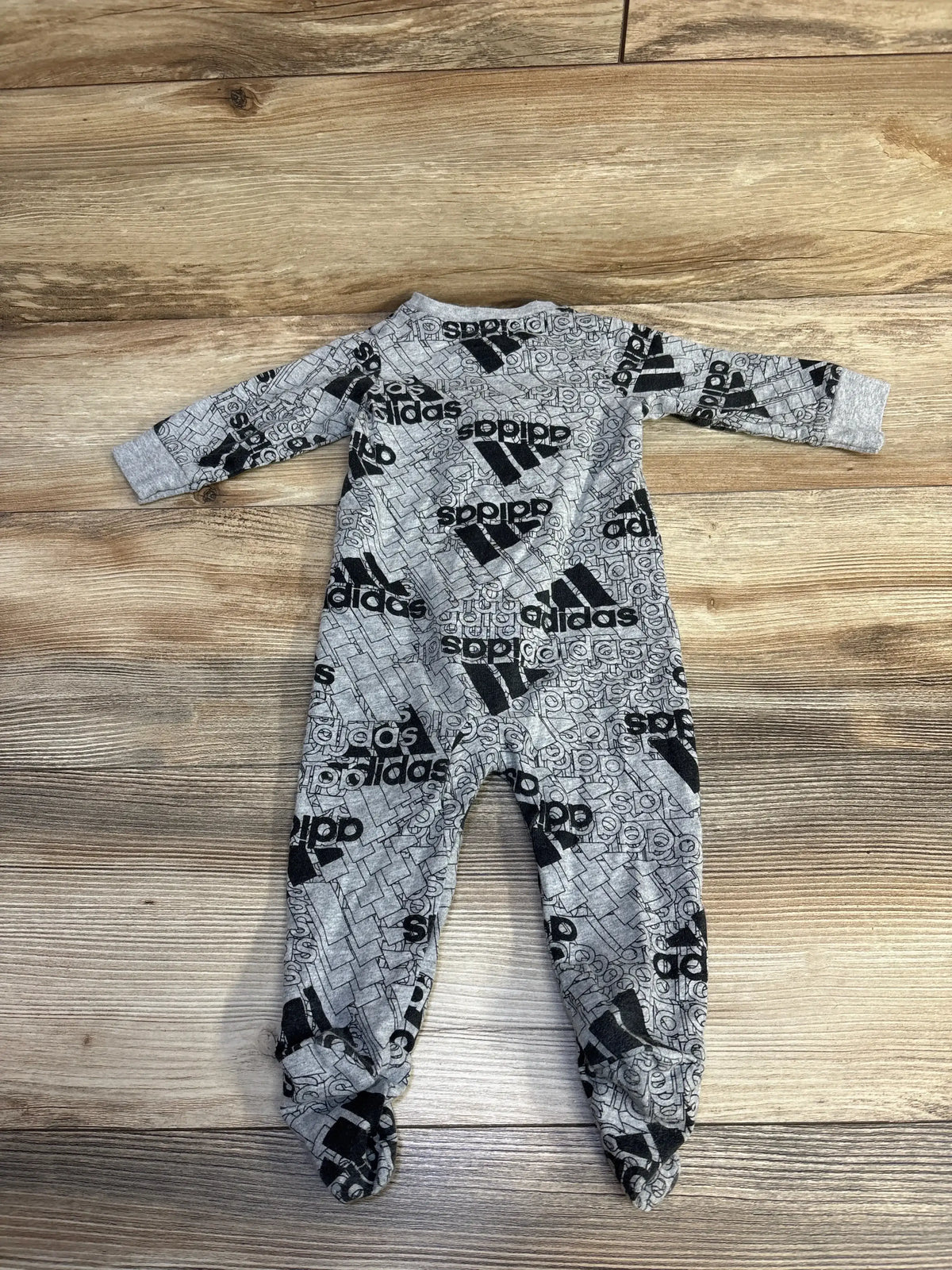 Grey Adidas baby onesie with black logo print laid flat on wood floor background