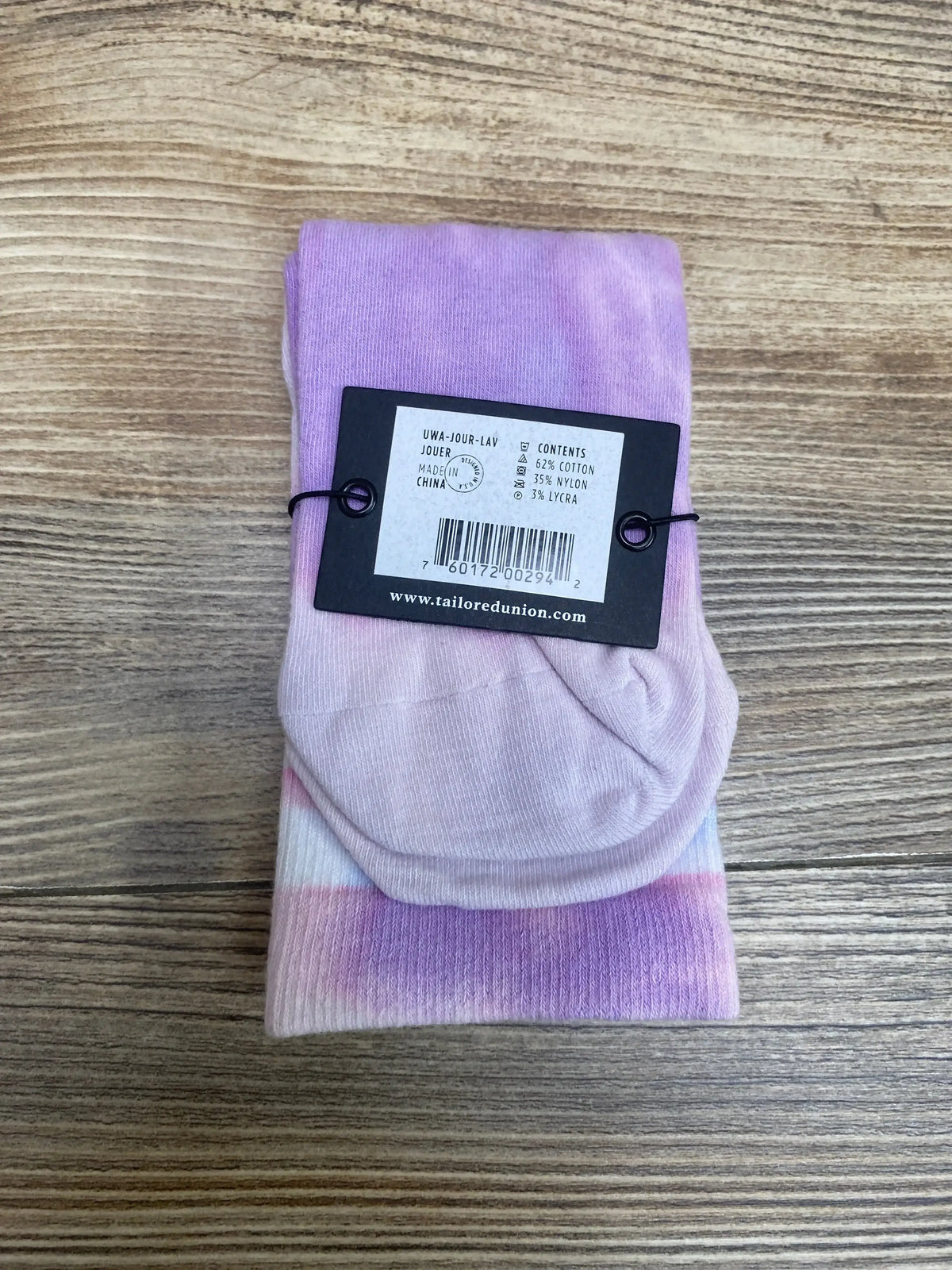 Top down view of folded purple and pink toddler socks showing Tailored Union hang tag with fabric content text on wood floor