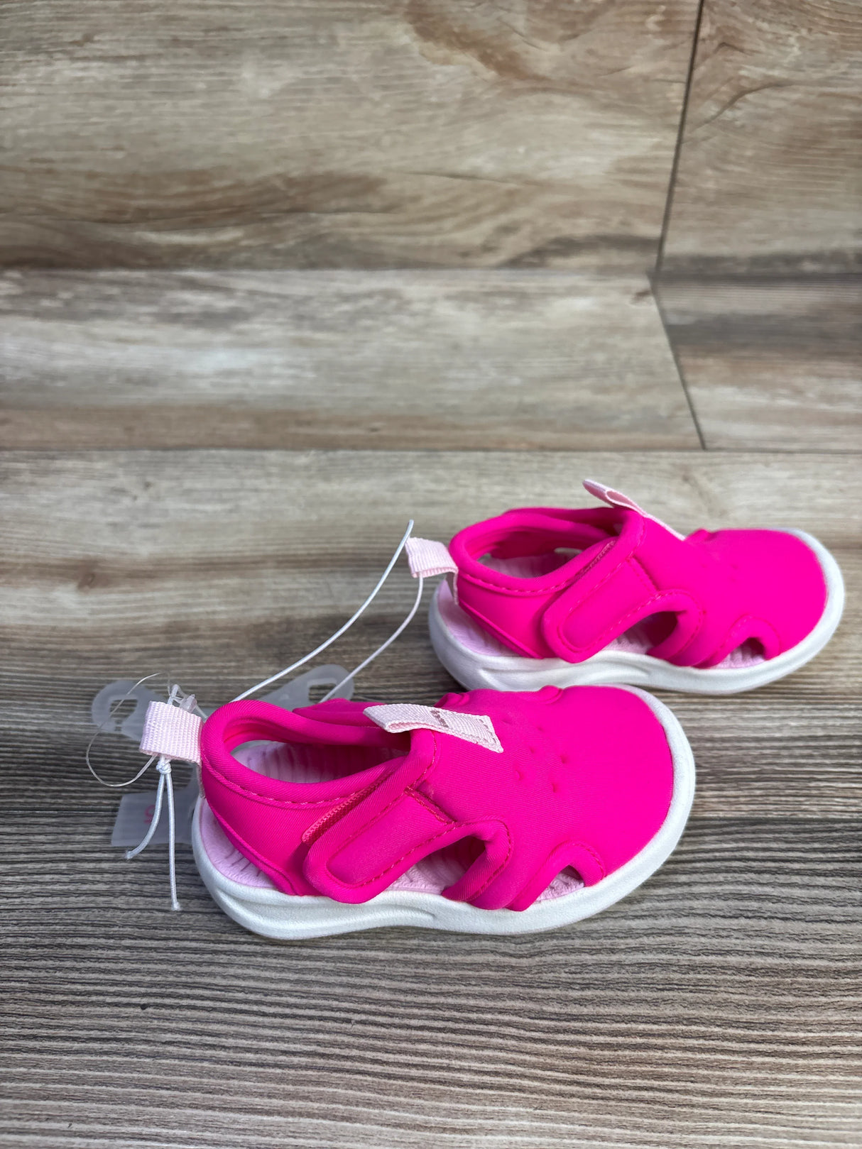Side view of Cat and Jack water shoes in bright pink, showing hook-and-loop straps and white cushioned sole on wood floor