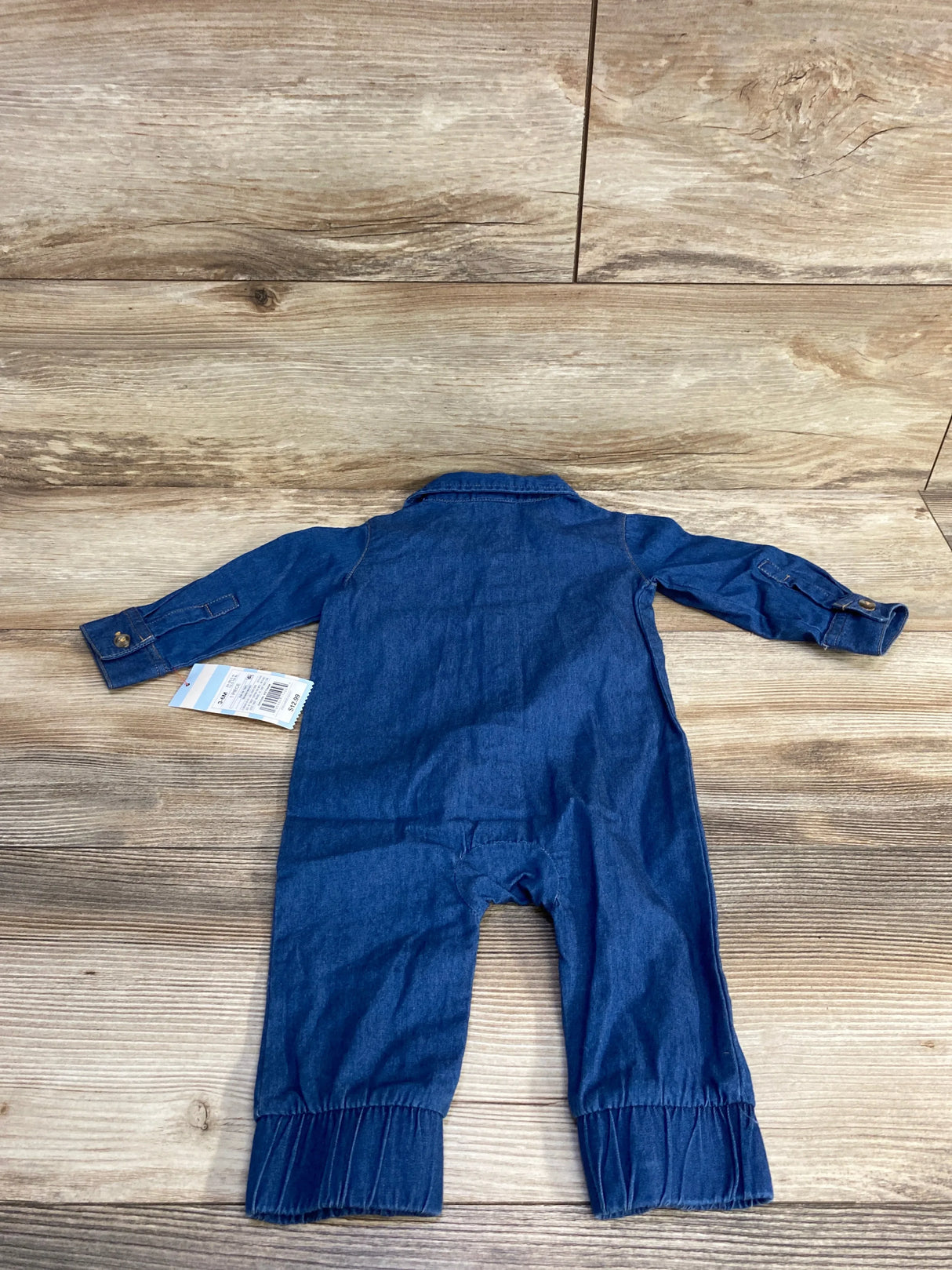 Baby denim jumpsuit with long sleeves and elastic cuffs on wooden floor