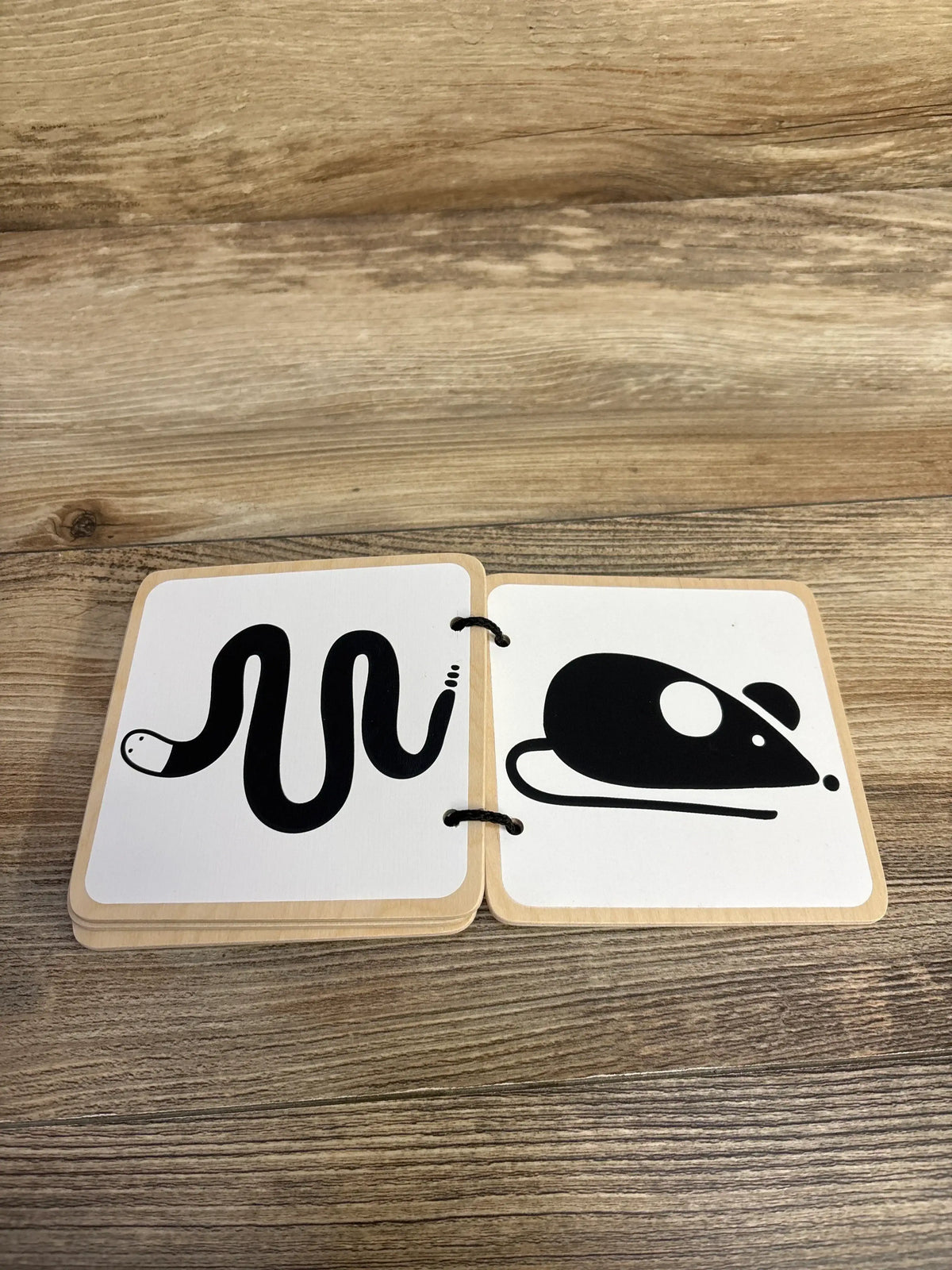 Open view of Lovevery wooden book showcasing high contrast black snake and mouse illustrations bound with rings on wood plank floor