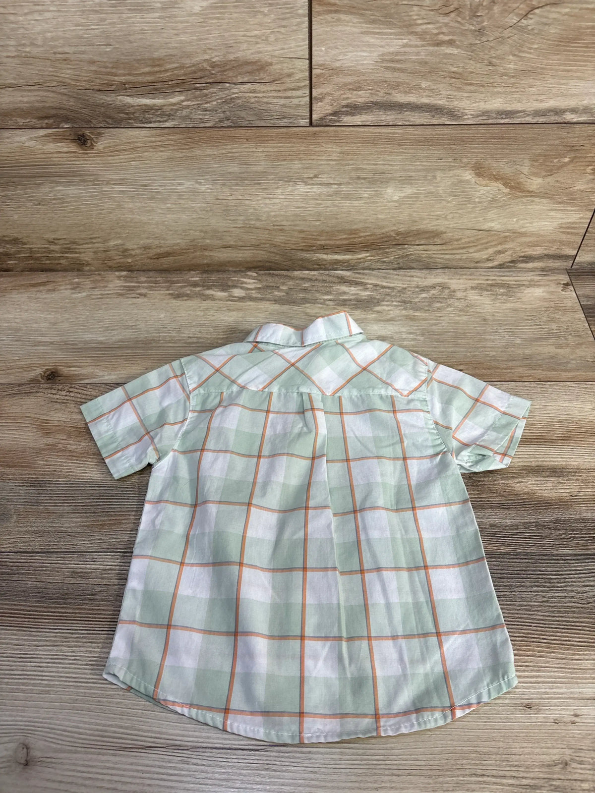 Back view of green and white plaid button-up shirt with orange windowpane lines, short sleeves and back pleat on wood floor