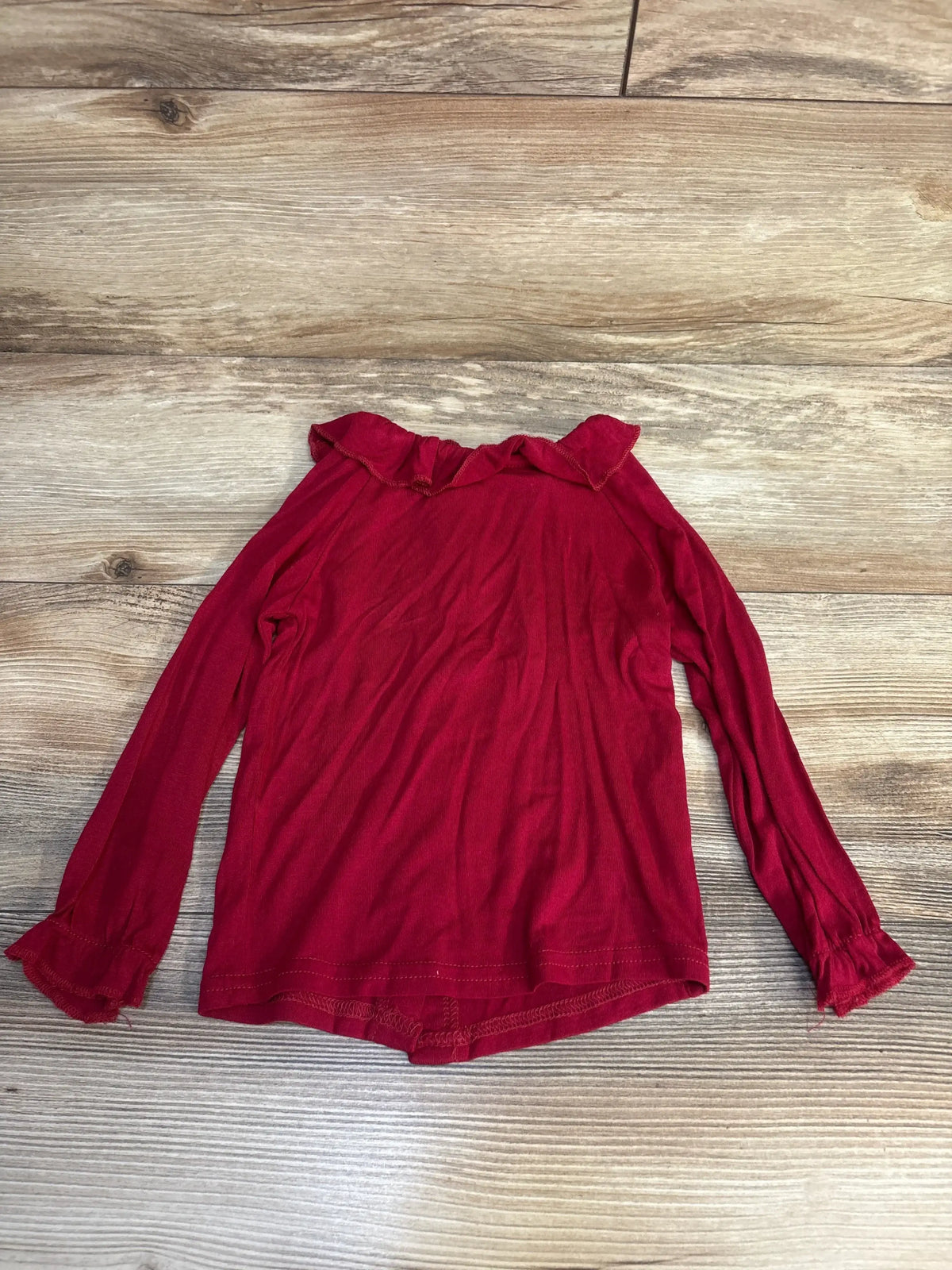 Red long sleeve girls shirt with ruffle collar and cuffs on wood background
