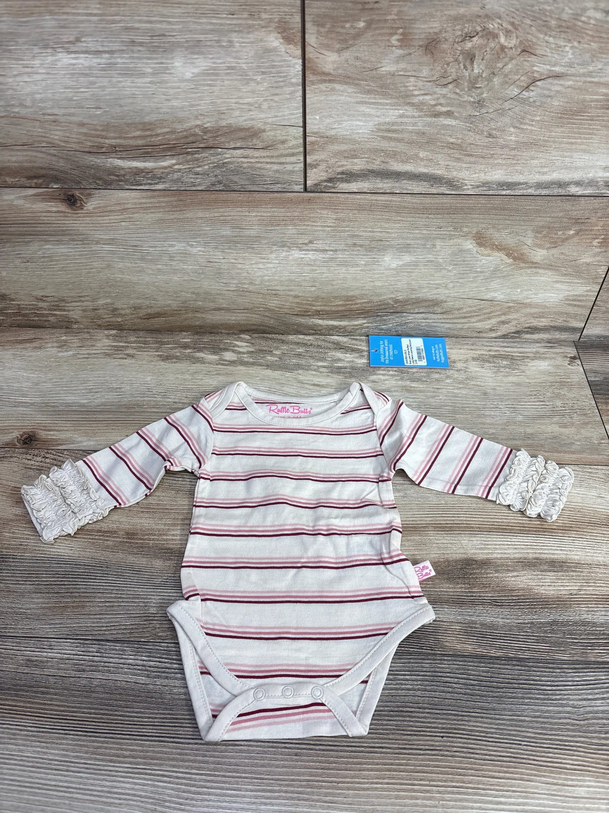 Striped long sleeve baby bodysuit with ruffle cuffs, snap closure, and tag on wood floor