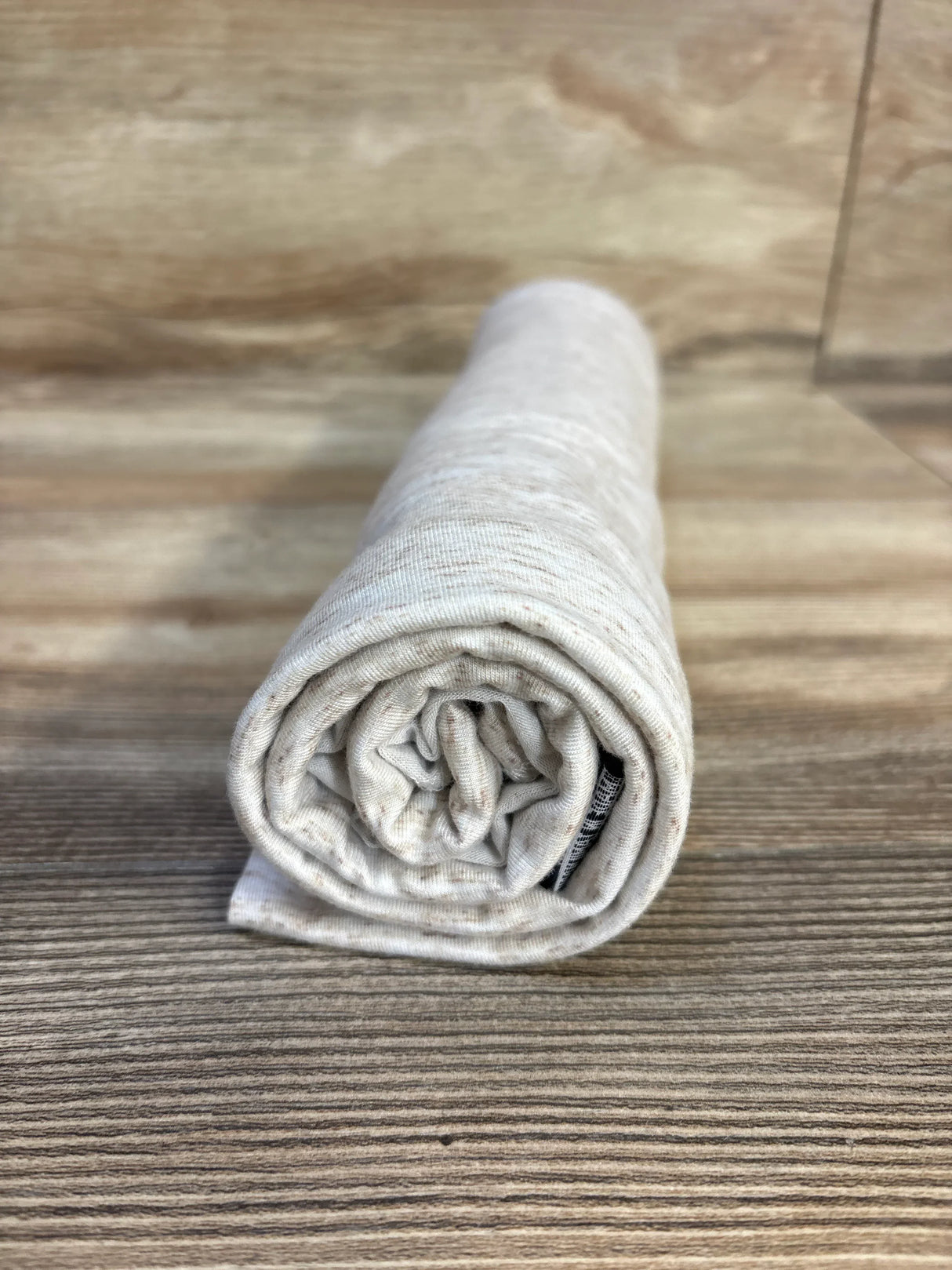Rolled beige kids clothing with subtle speckles, soft fabric on wood floor