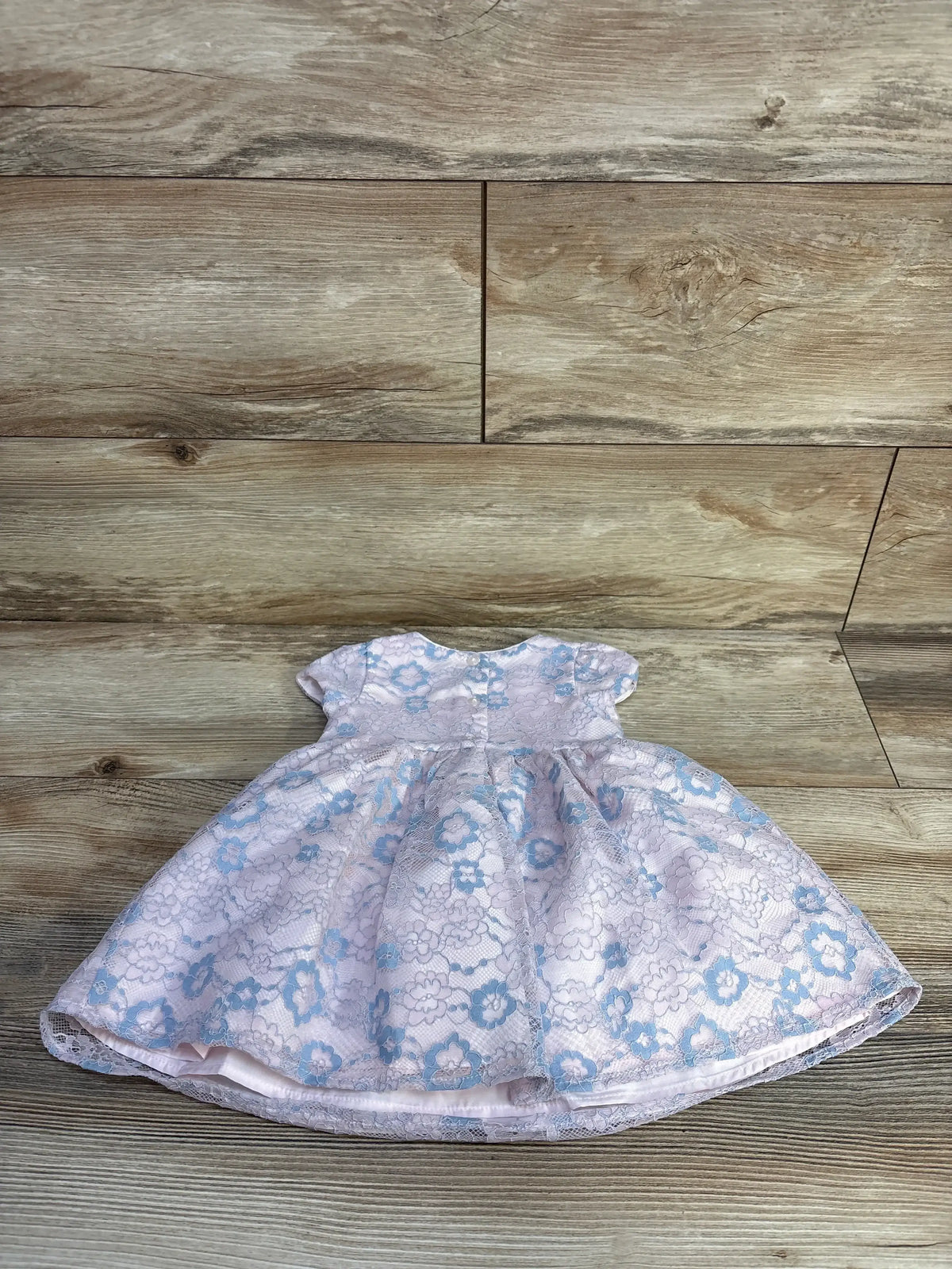 Pink baby dress with blue floral lace overlay and short sleeves on wood floor