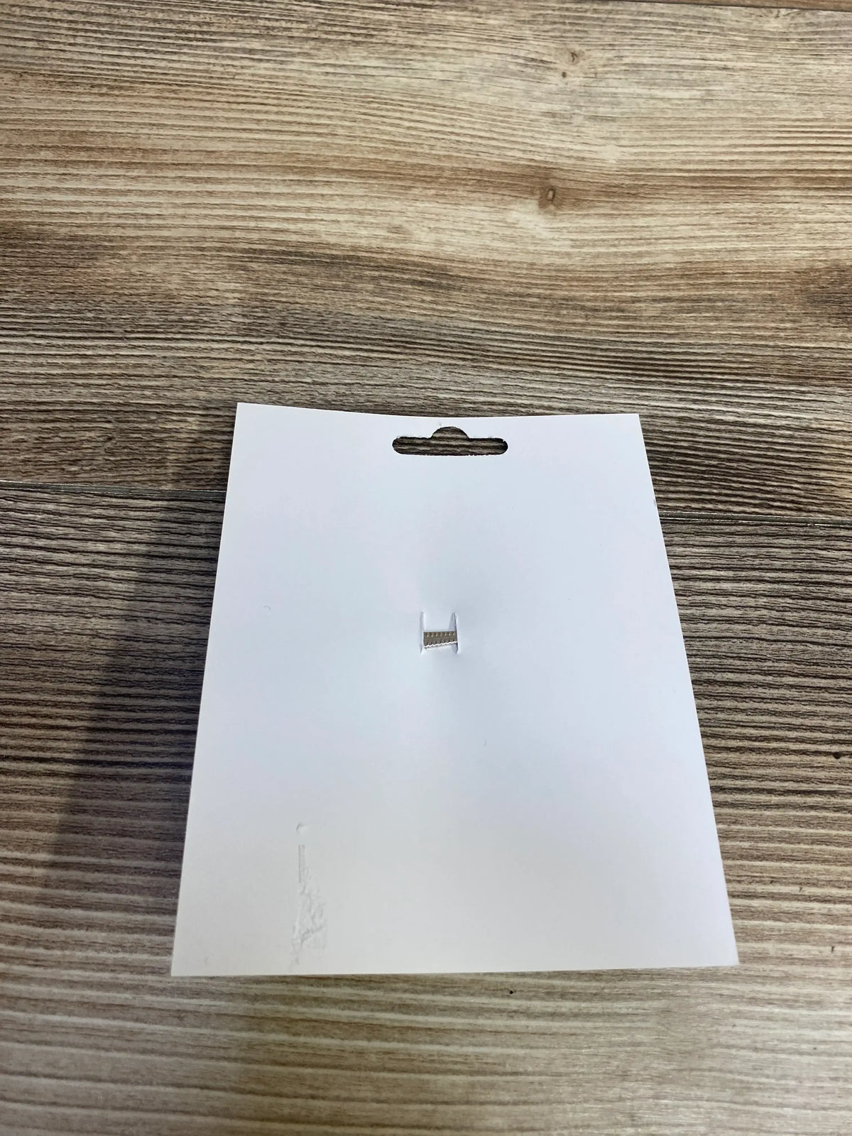 Blank white product tag with hang hole on wood surface, for kids and maternity items