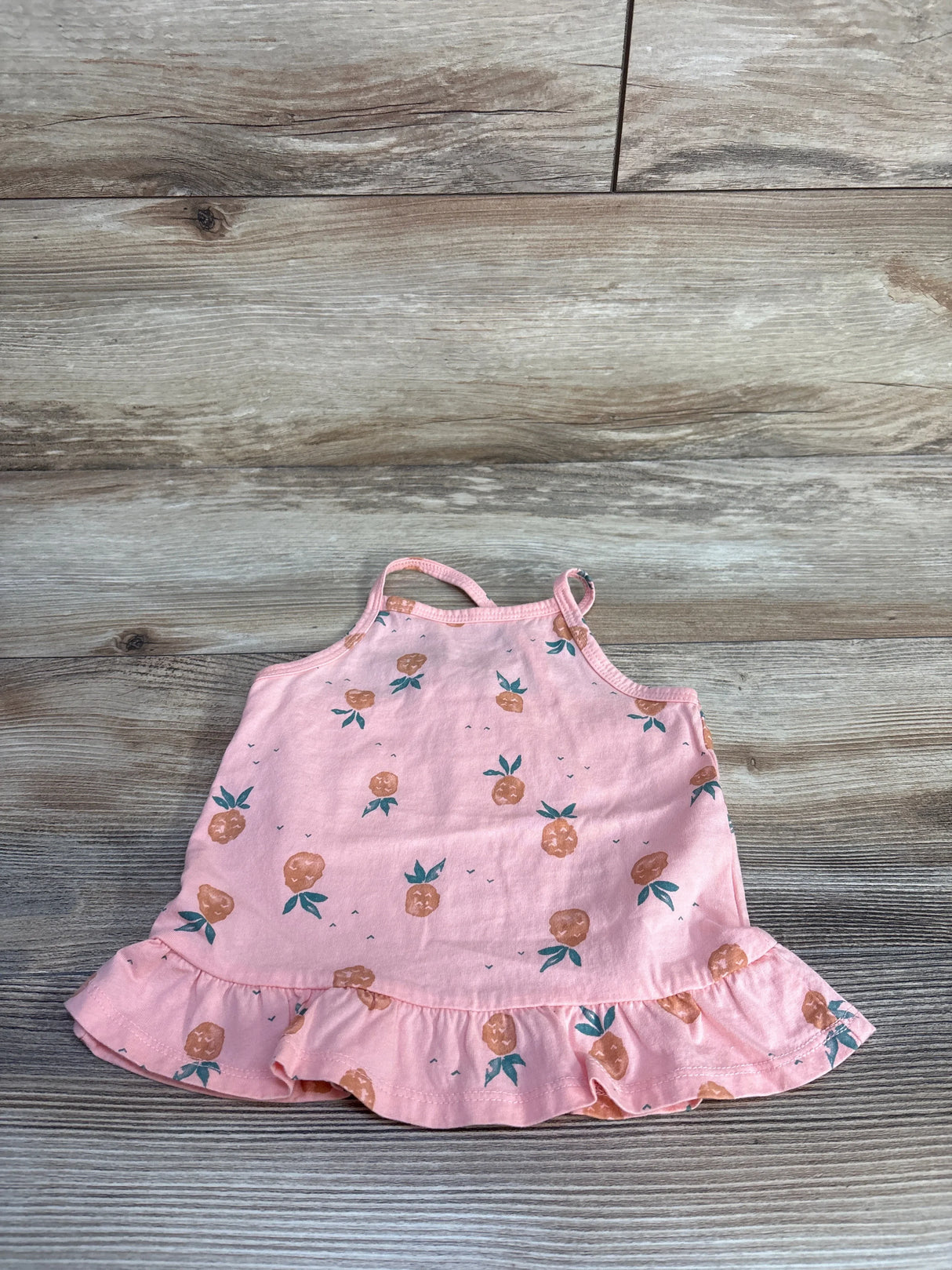 Flat lay of Oshkosh pink pineapple print toddler ruffle tank top 24 months with ruffled hem and thin straps on wood