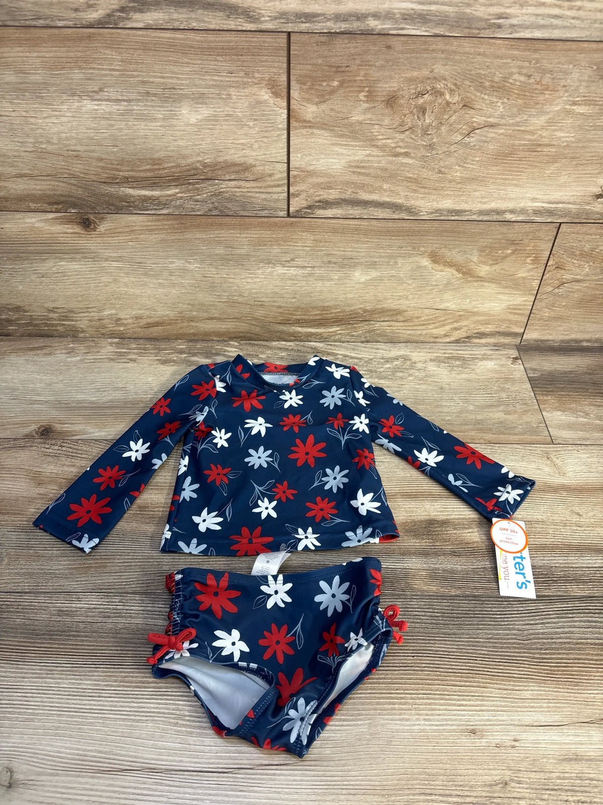 Front view of navy floral rash guard and bikini bottoms showcasing long sleeves and round neck with wood flooring background