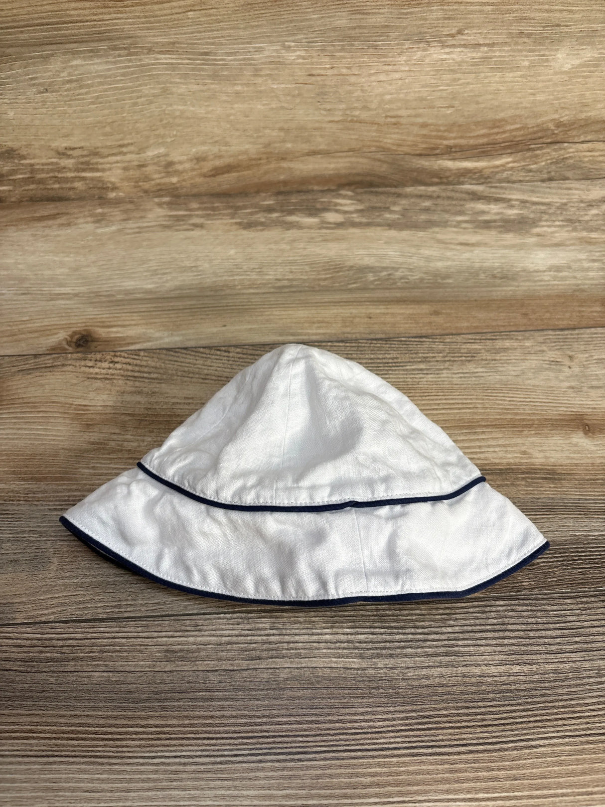 White linen bucket hat with navy blue trim on wooden surface