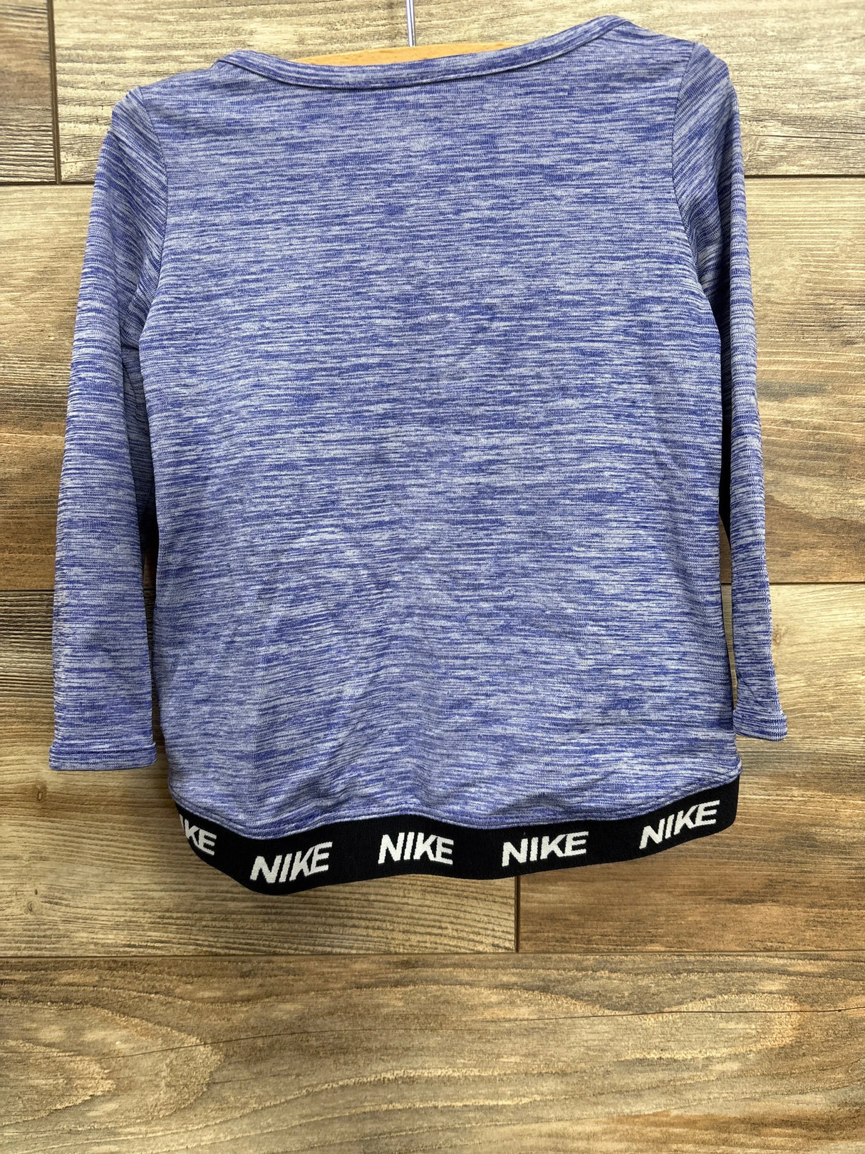 Heather blue Nike long sleeve crop top with black elastic waistband featuring white Nike logo on wood background