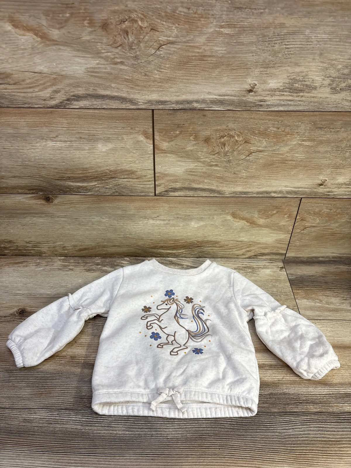 Front view of Kids Headquarters ivory unicorn pullover sweatshirt with floral unicorn design on wood background