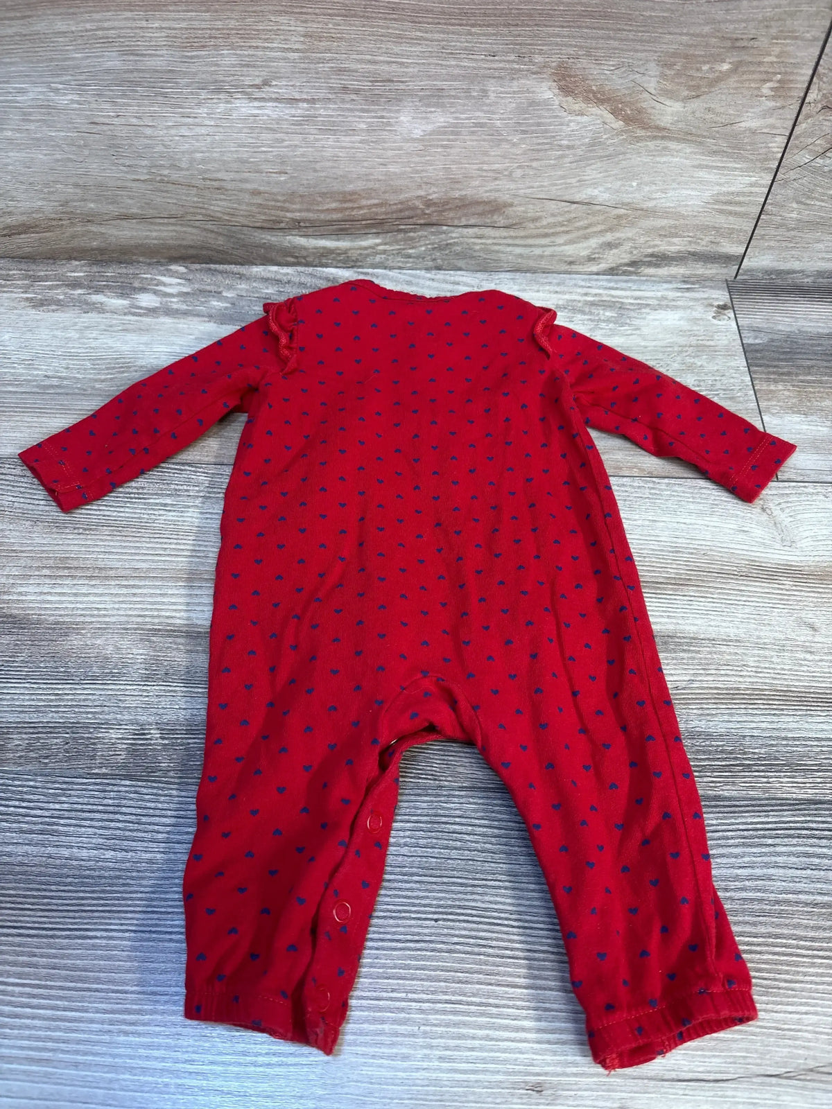 Red baby romper with blue heart print, long sleeves, laid flat on wood background