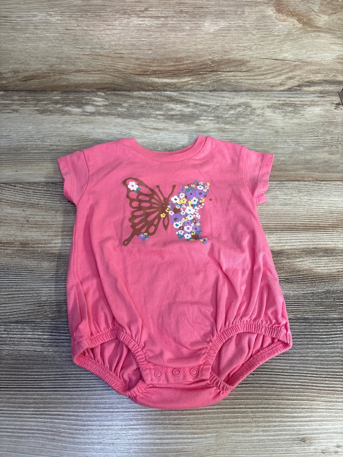 Front view of pink Okie Dokie butterfly bubble romper showcasing its floral butterfly design on a wood-grain background