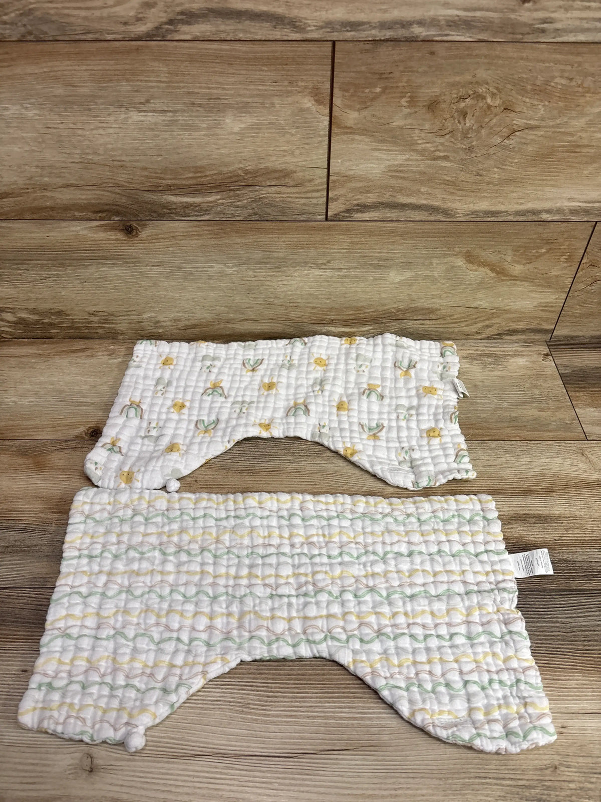 Two white muslin burp cloth bibs with a colorful pattern on a wooden background