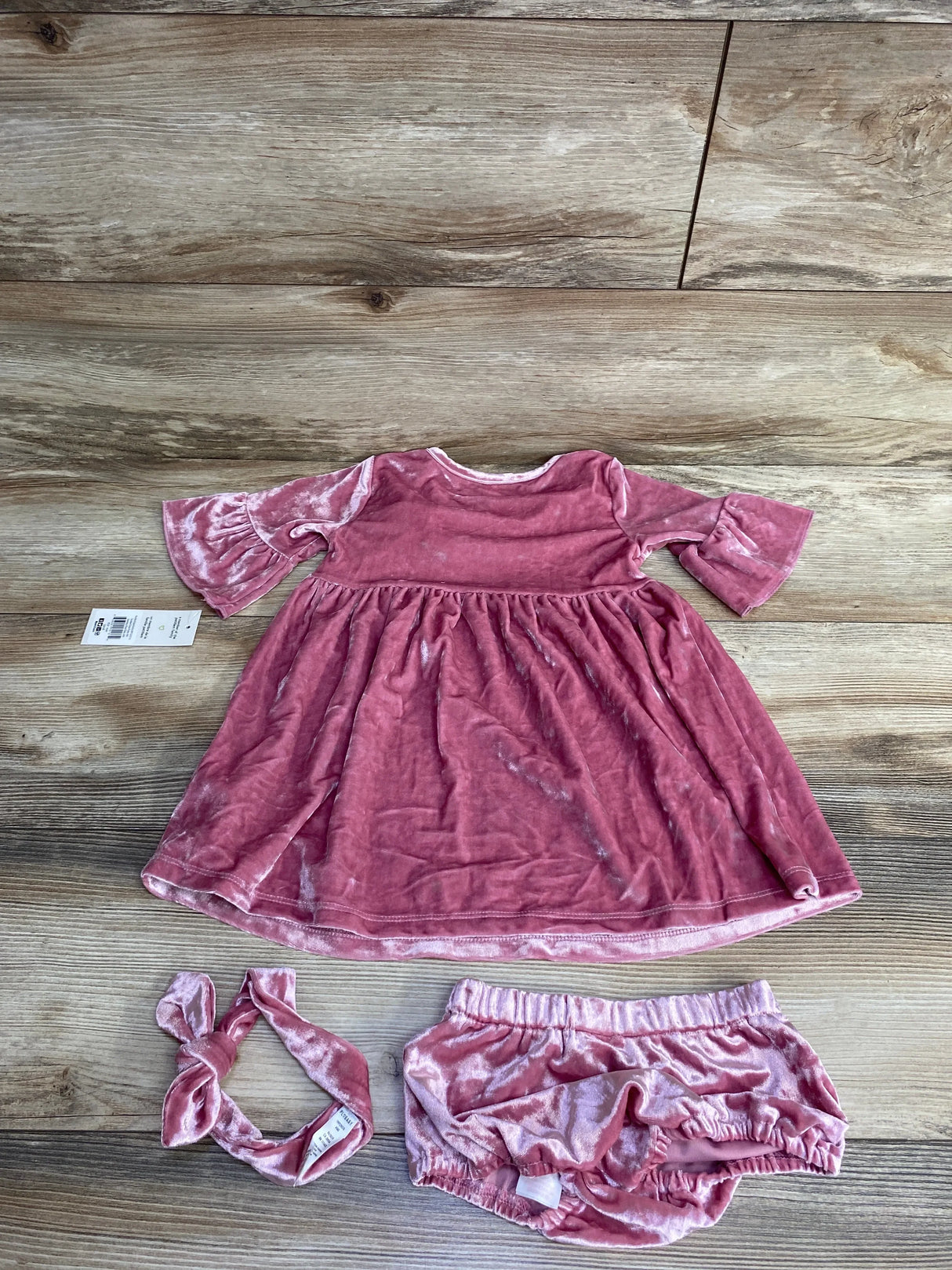 Pink velvet baby dress set with matching bloomers and headband on wood floor