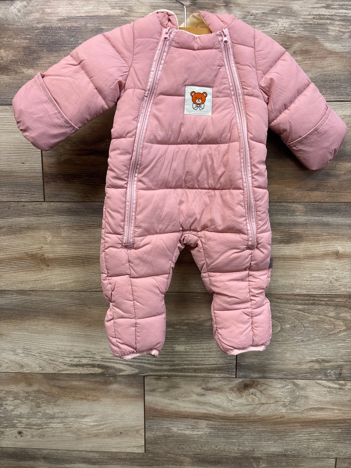 Front view of pink fleece-lined baby snowsuit showcasing dual front zippers and fold-over sleeve cuffs on wood background
