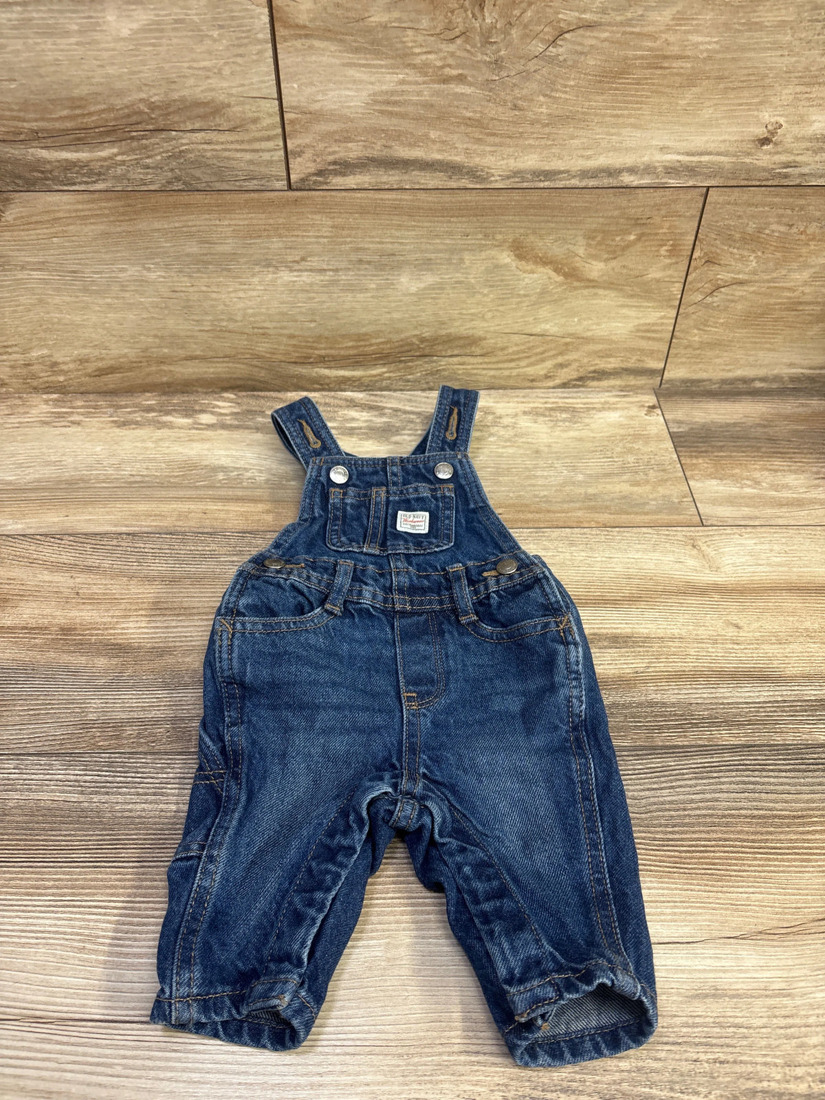 Front view of Old Navy Workwear Denim Overalls in blue, size 0-3m, with bib pocket and adjustable straps on wood flooring