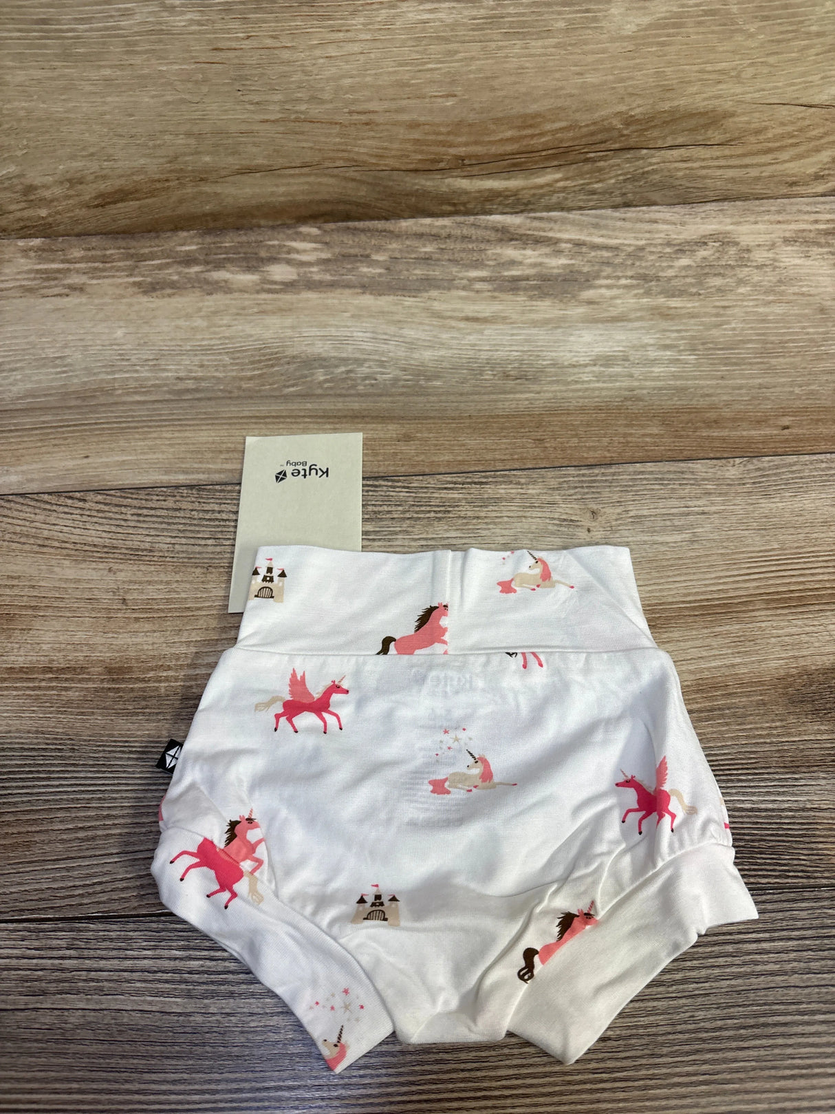 Flat lay of Kyte Baby bamboo bummie showcasing pink unicorn print on white fabric, size 3-6 months on wood background