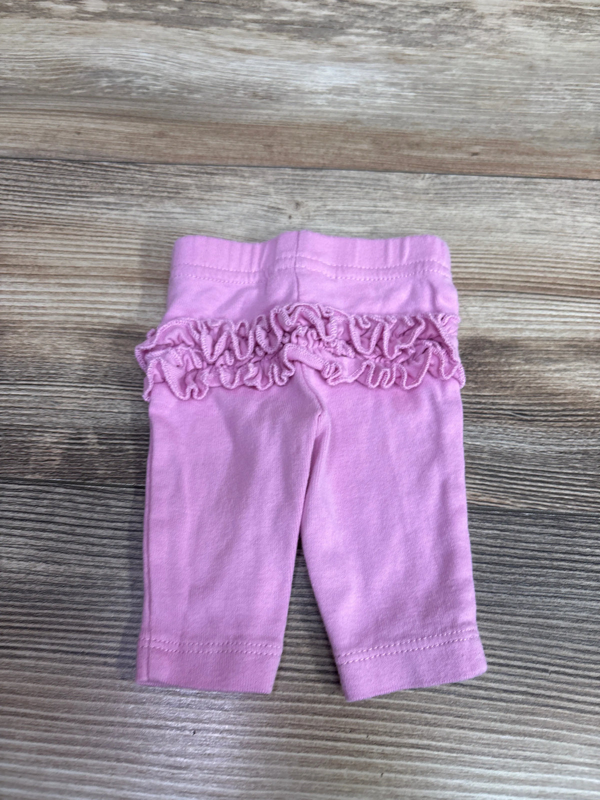 Front view of pink Child of Mine baby pants in preemie size showcasing a ruffled waistband on a wood surface