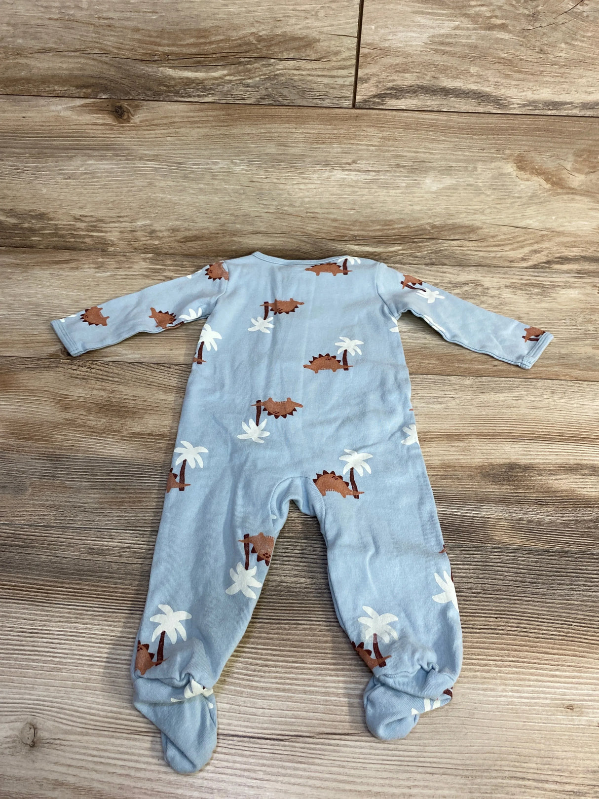 Back view of Carter's Dino sleeper, size 6M, light blue with brown dinosaur and white palm tree print, footed long-sleeve design on wood background