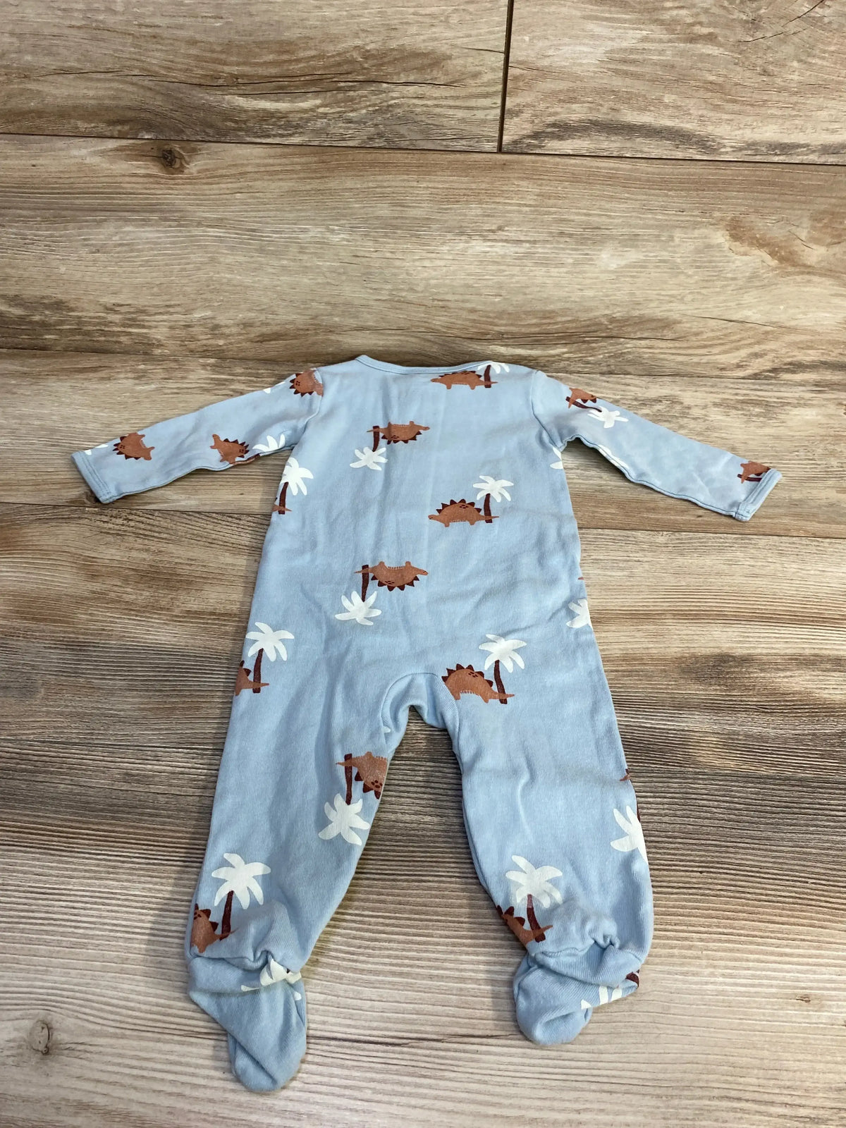 Back view of Carter's Dino sleeper, size 6M, light blue with brown dinosaur and white palm tree print, footed long-sleeve design on wood background