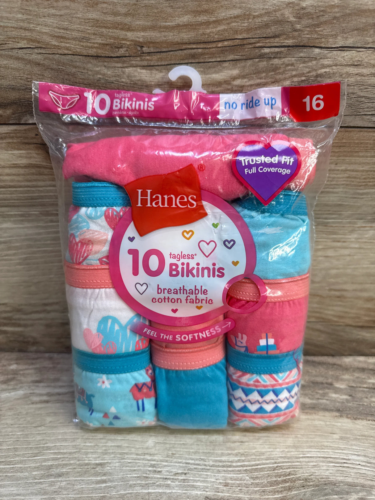 Front view of Hanes girls’ tagless bikini underwear 10-pack (size 16) showing assorted pink and teal patterns and packaging on a wood background