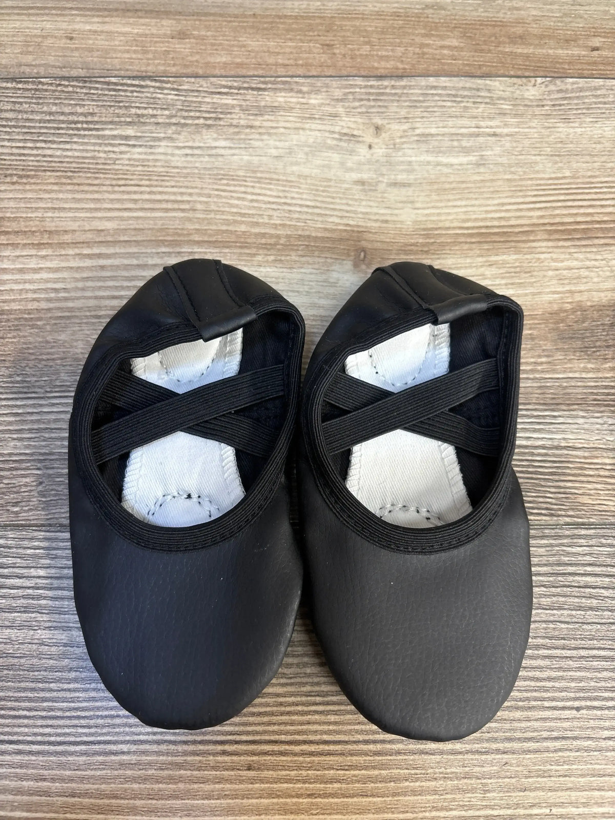 Black toddler ballet flats with elastic straps on wood background