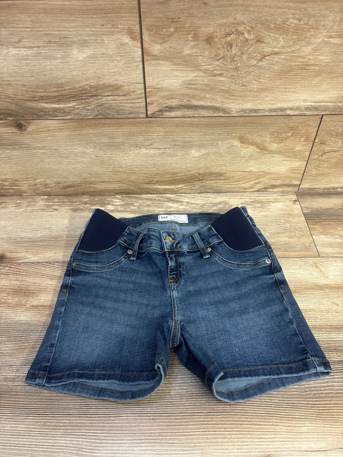 Front view of Gap maternity denim shorts showcasing dark wash blue stretch denim and inset panels on a wood floor