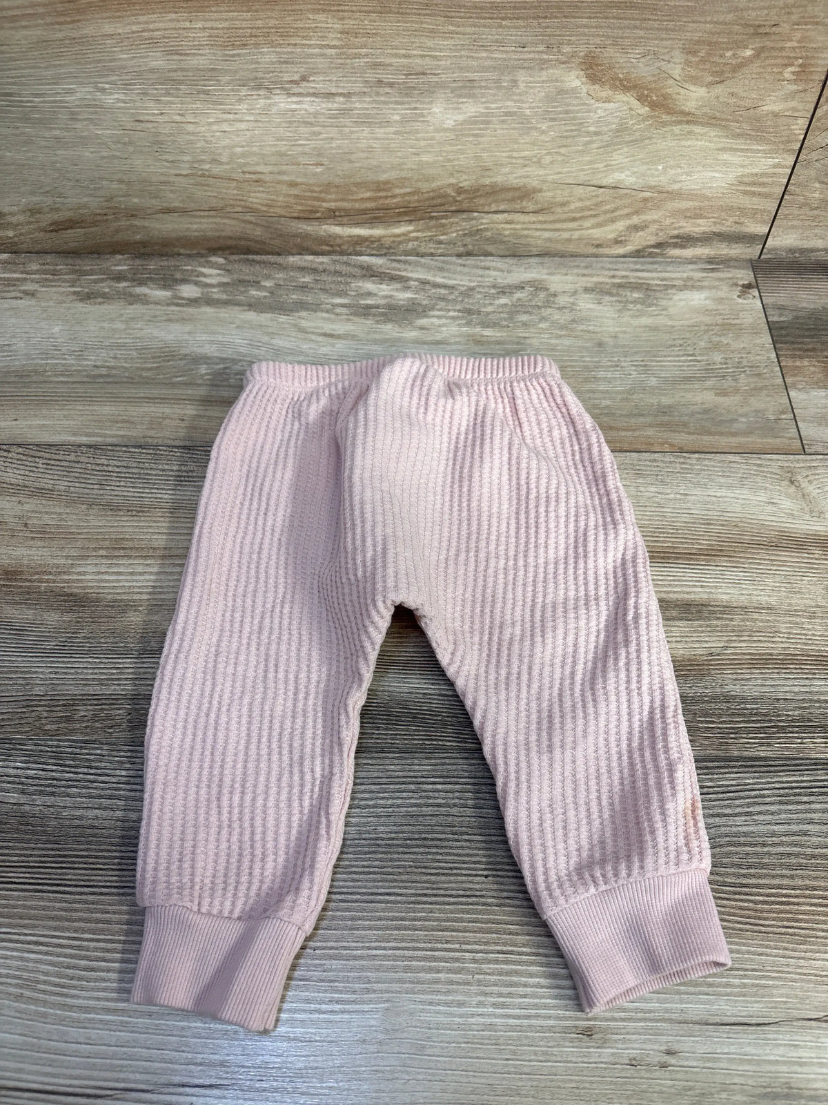 Flat lay of pink thermal waffle-knit baby jogger pants showing elastic waistband and ribbed cuffs on light wood floor