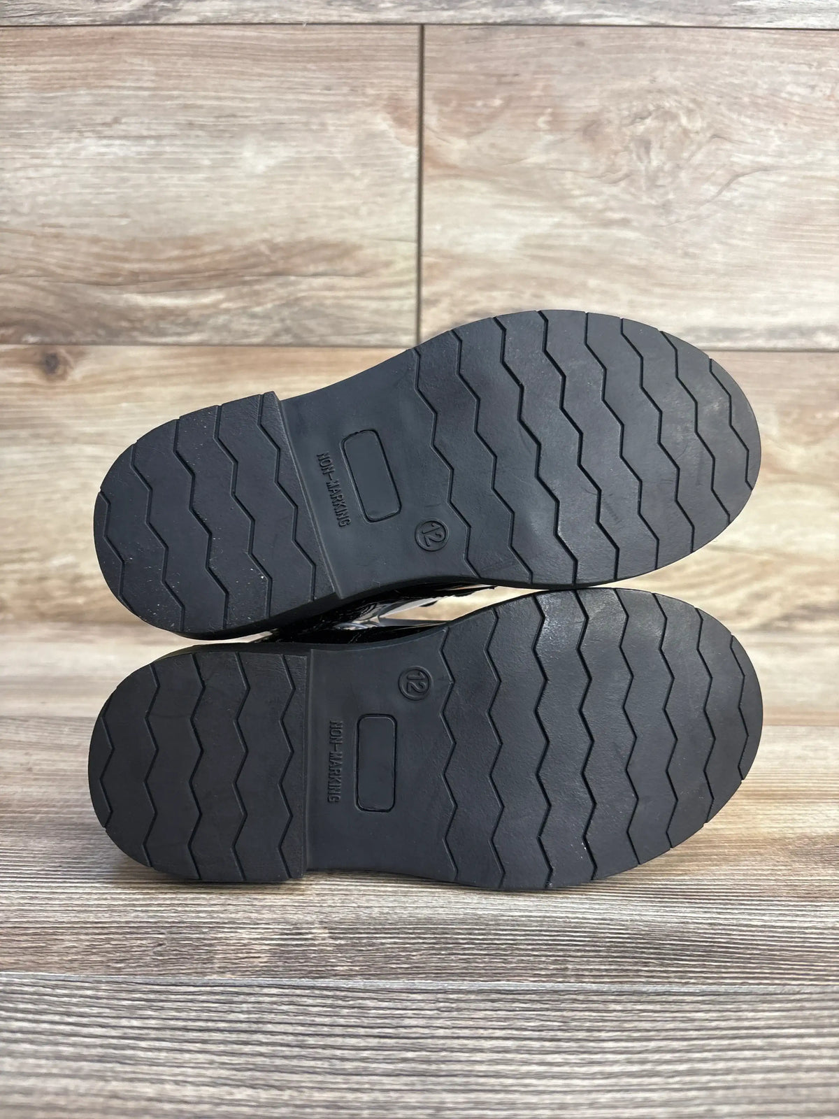 Bottom view of Gymboree toddler lace-up boots showing black non-marking rubber soles with zigzag tread and size 12 marking on wood floor
