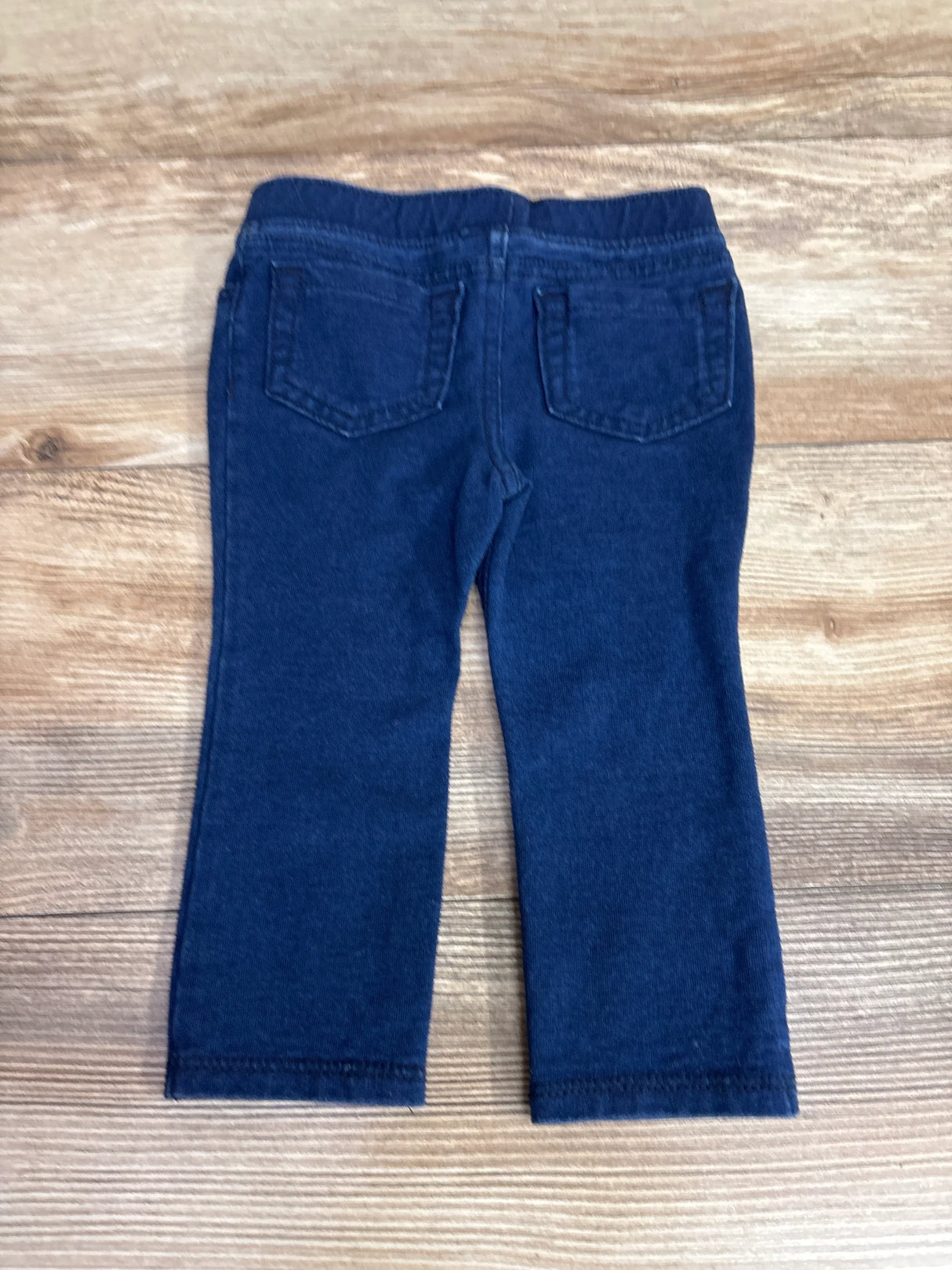 Back view of dark blue kids' denim jeggings with pockets on wood background