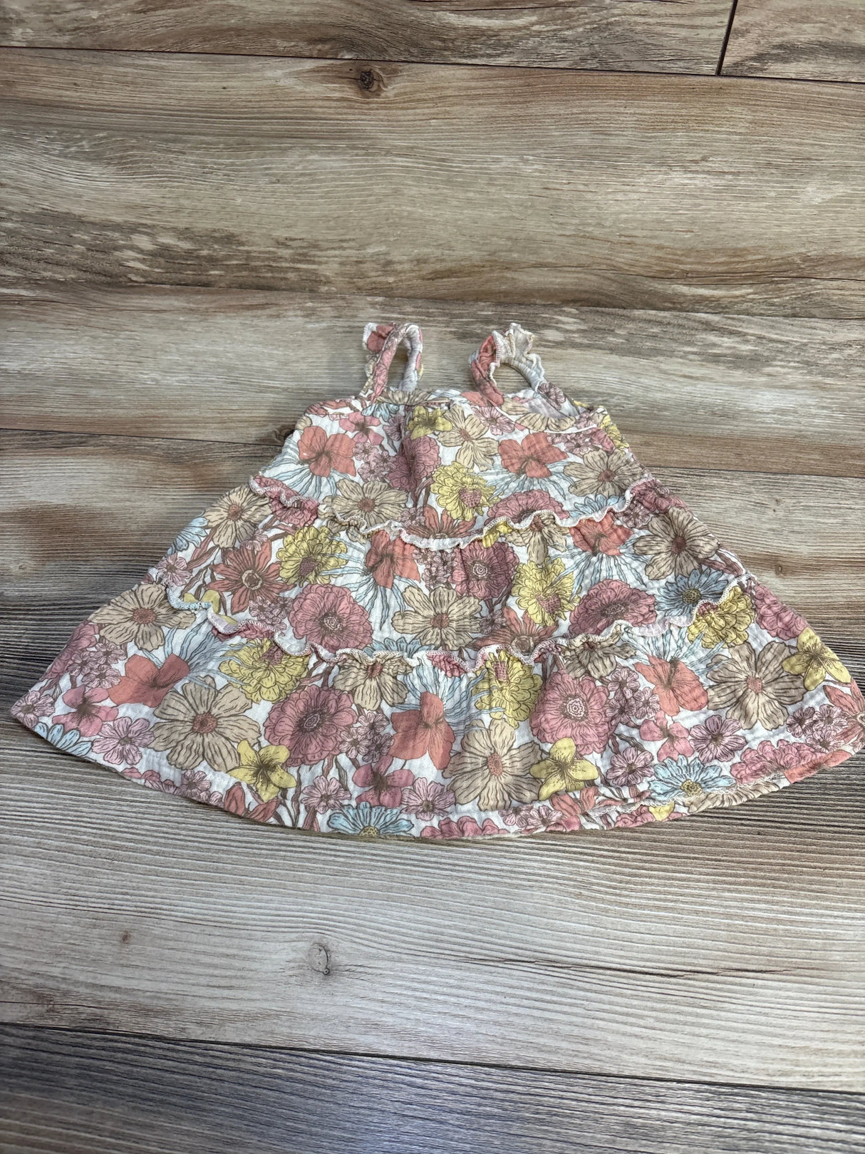 Top-down view of Rabbit + Bear floral toddler dress 18m showing ruffled tiered skirt and shoulder straps on wood floor background