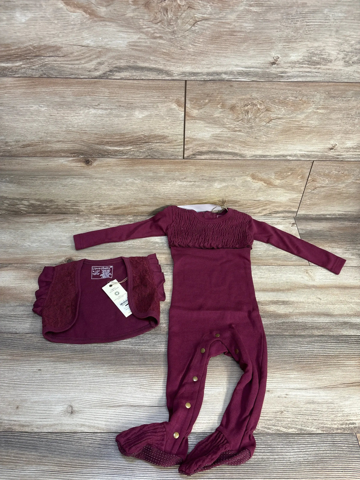 Top-down view of cranberry L'oved Baby smocked footie with matching lace ruffle vest, long sleeves and snap leg closures on wood floor