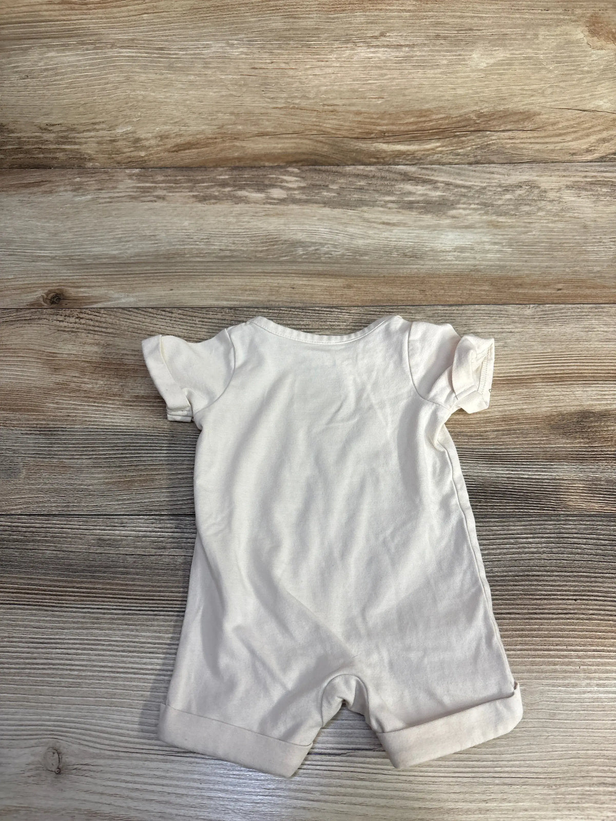Back view of Cat and Jack Oh Hey Boo newborn shortie romper in ivory with short sleeves and cuffed legs on wood grain