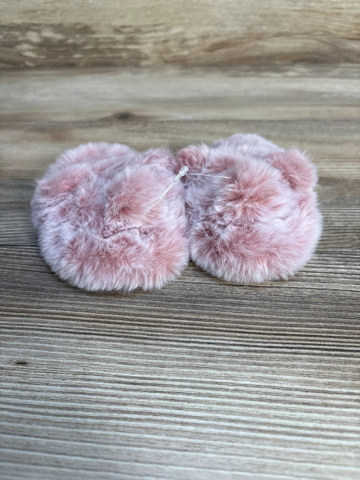 Soft pink faux fur baby booties on wood background, kids footwear resale.